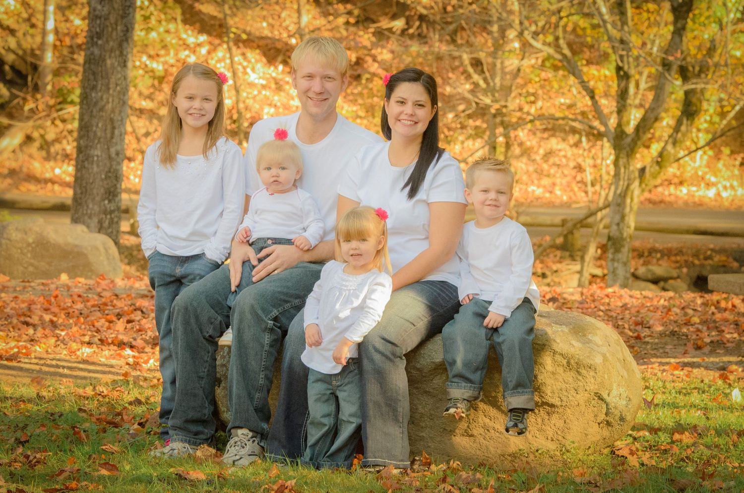A family sits together on a large rock in an autumn forest setting with fallen orange leaves surrounding them in Pigeon Forge TN.