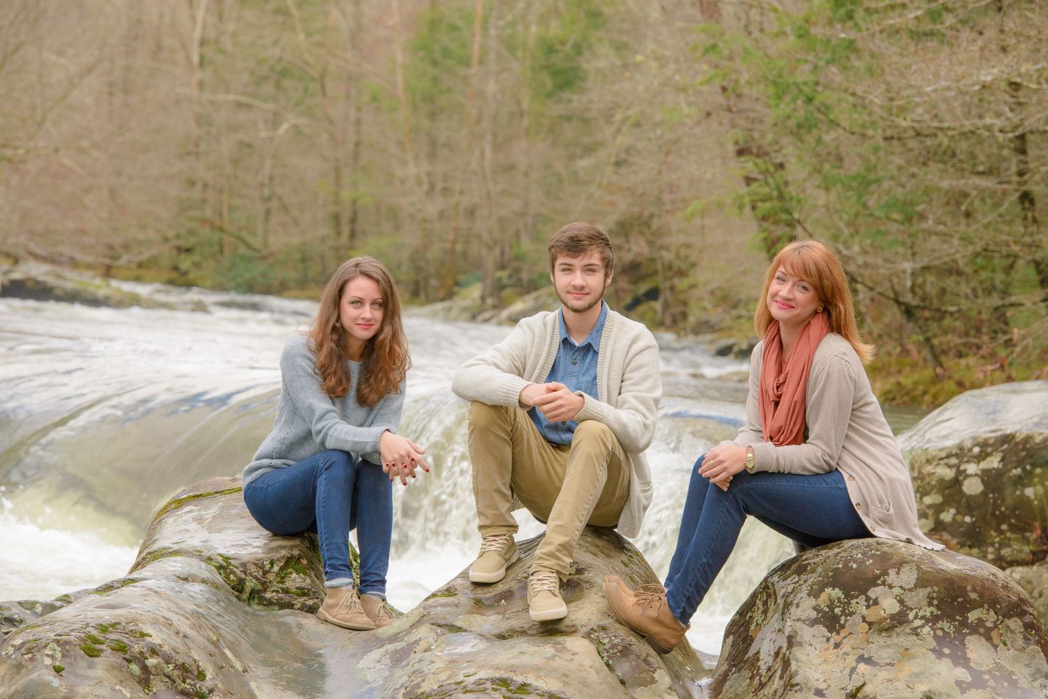 Three people sitting together on large rocks by a rushing waterfall in a natural outdoor setting by Sevierville Photographers.