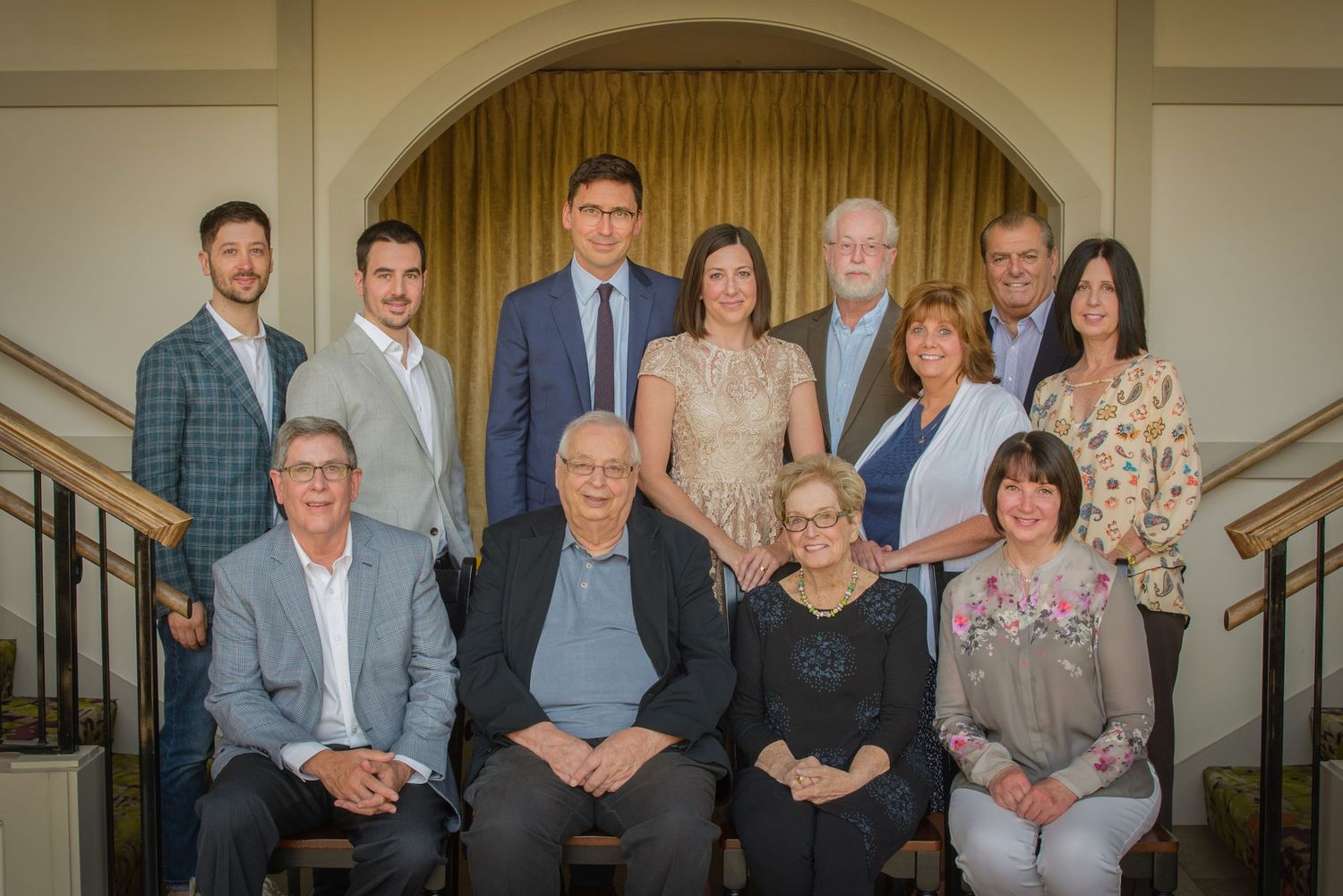 A formal group portrait of twelve people arranged in two rows in front of an arched doorway at Dollywood's DreamMore Resort.
