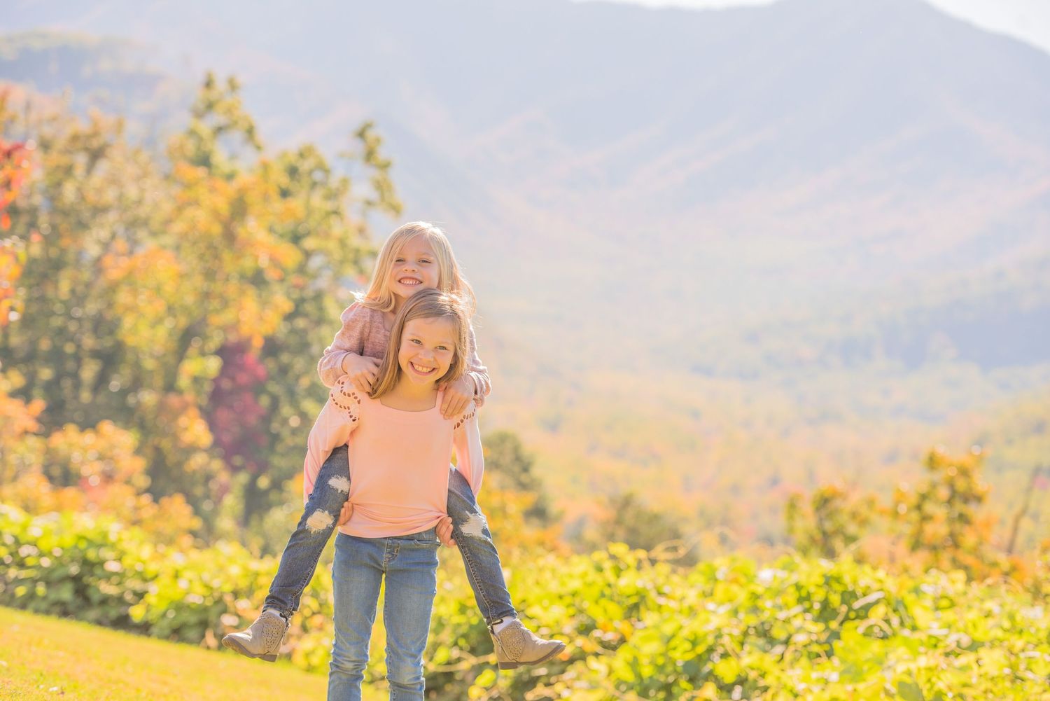 Two kids enjoy a playful piggyback ride outdoors against a backdrop of the Great Smoky Mountains and golden foliage in Sevierville TN.