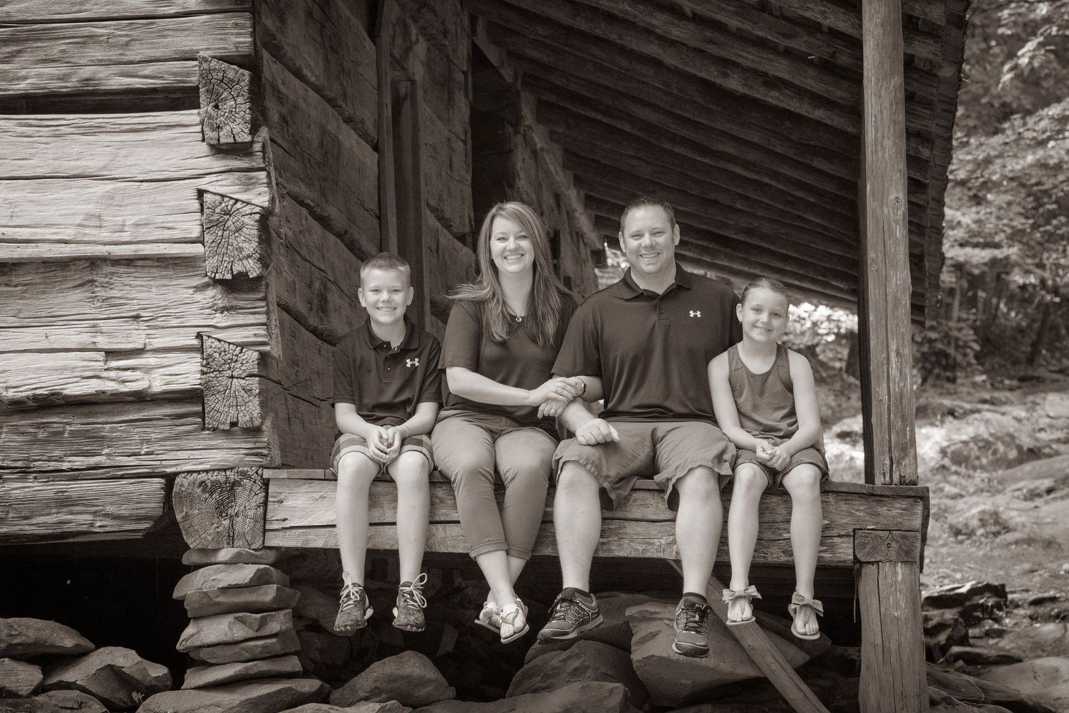 A family sits together on the porch of an old rustic log cabin in a black and white photograph in the Great Smoky Mountains national park.