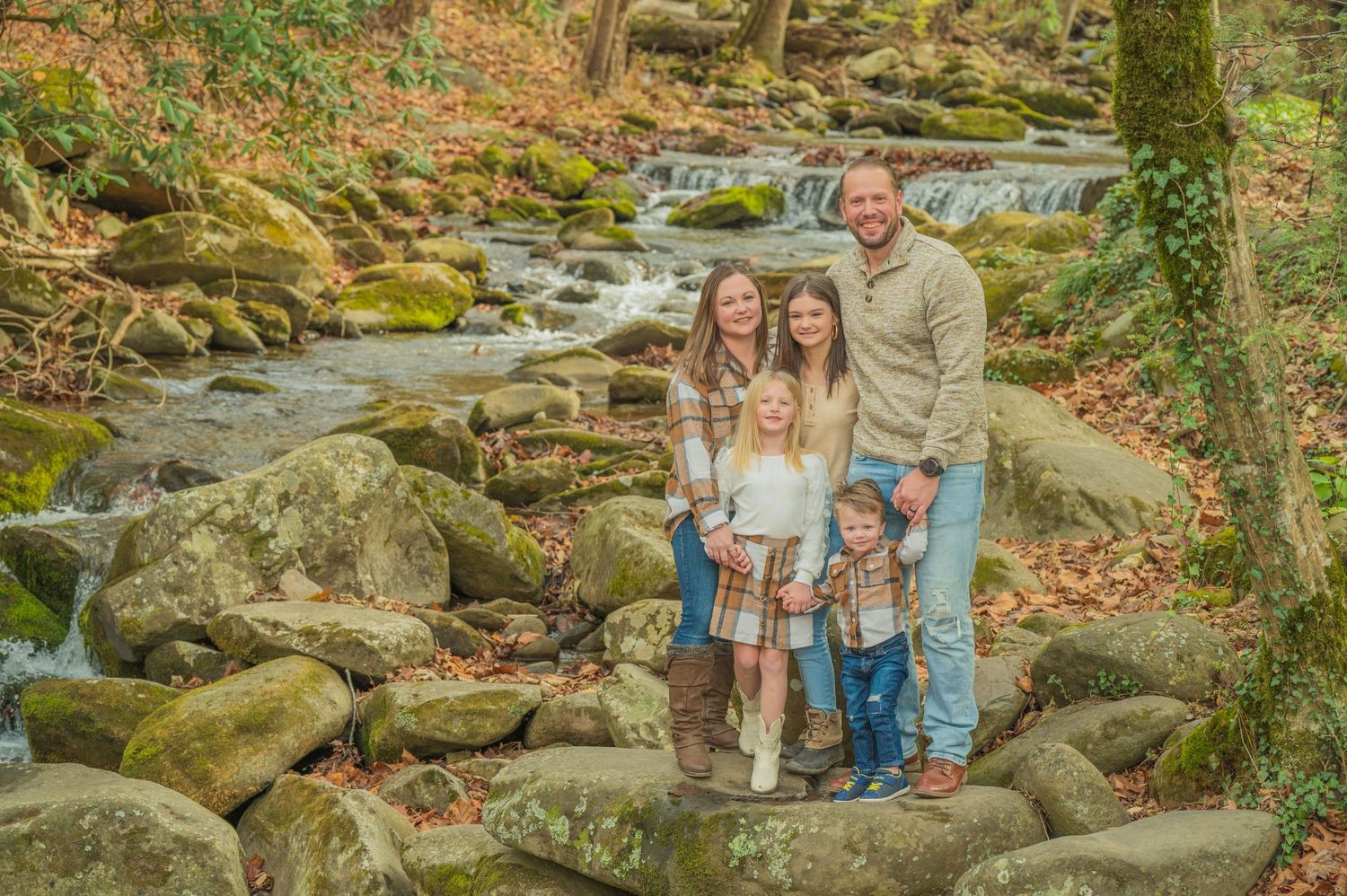 Family posing together by cascading stream with mossy rocks and fall foliage in woodland setting by Gatlinburg Photographer.