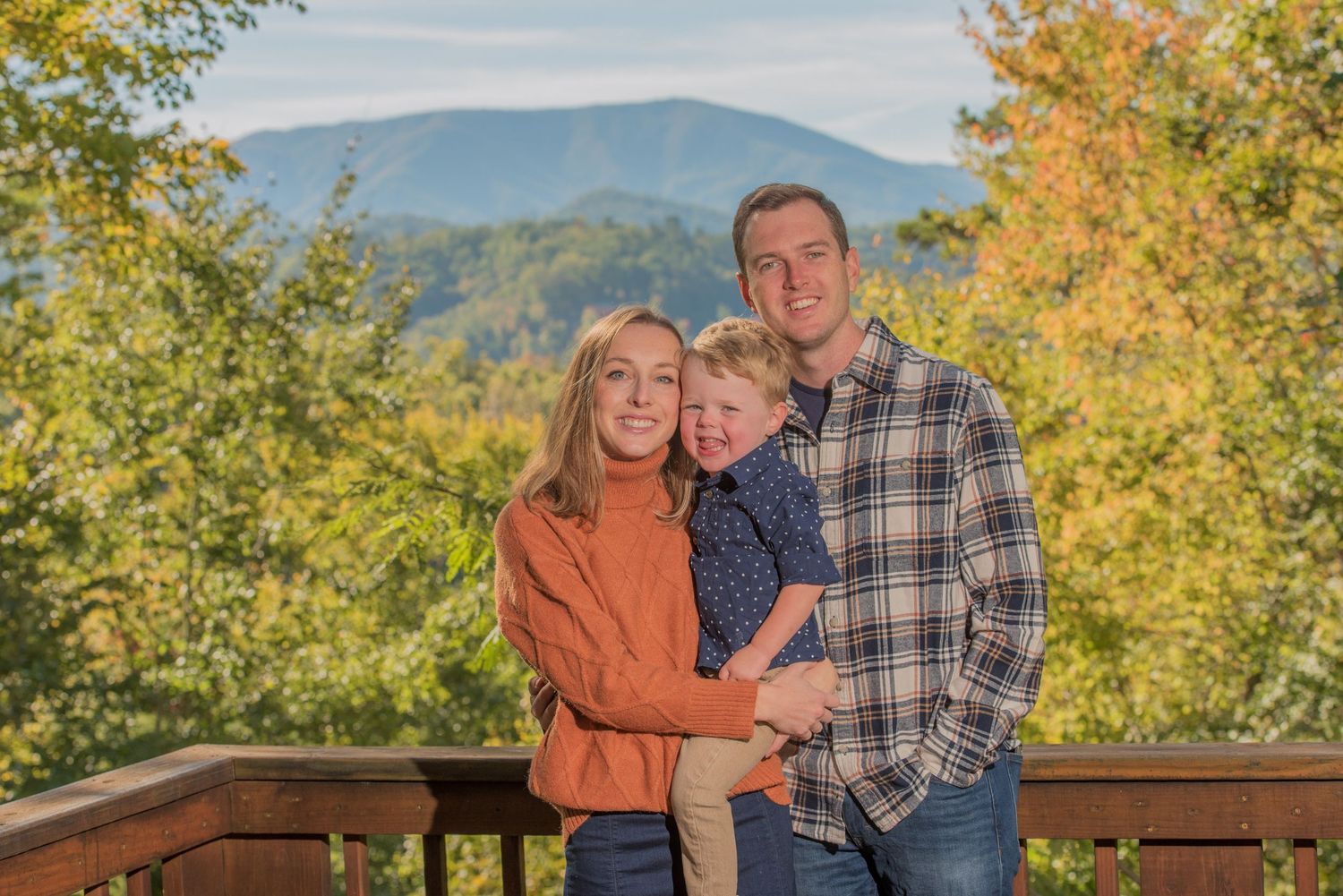 A family enjoys an autumn day on a deck overlooking mountains with fall foliage in the background with professional lighting.