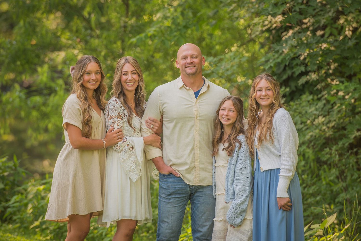 A family of five poses together outdoors on a sunny day with green foliage in the background Sevierville TN.