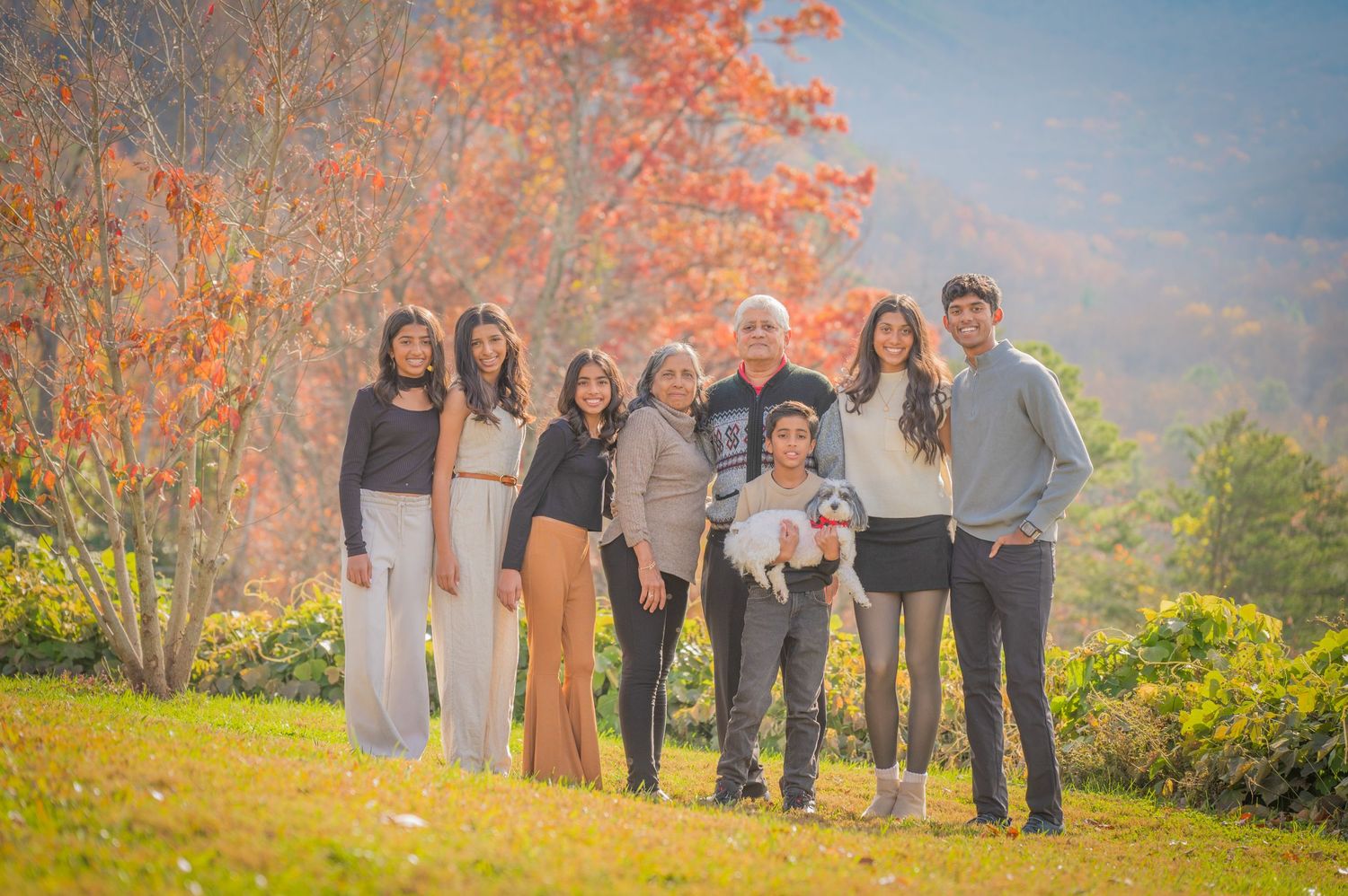 Gatlinburg TN photographers portrait of a family together outdoors on a grassy hill against autumn trees with vibrant orange foliage.