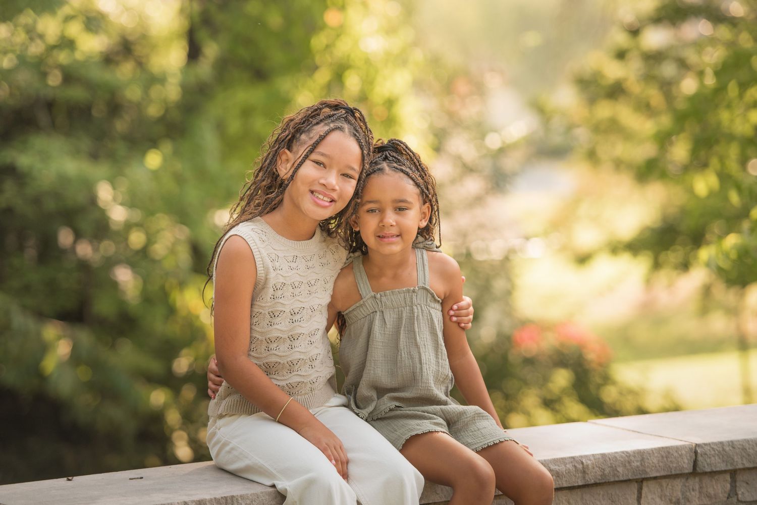 Children sitting together on a stone wall at sunset with a dreamy bokeh background and warm golden lighting by Gatlinburg TN photographers.