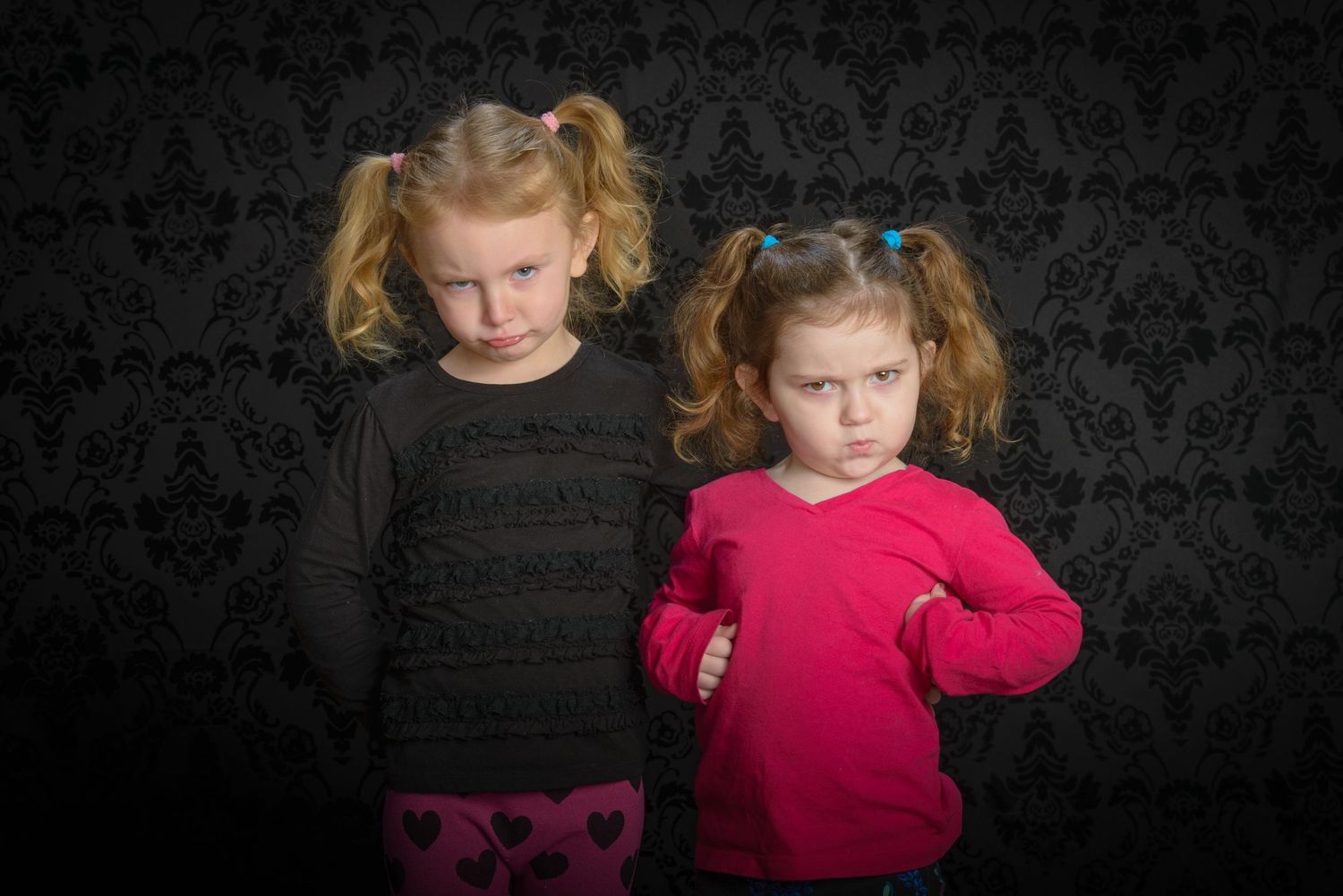 Two young children in contrasting black and pink tops pose against a dark patterned backdrop with Professional Studio Lighting.