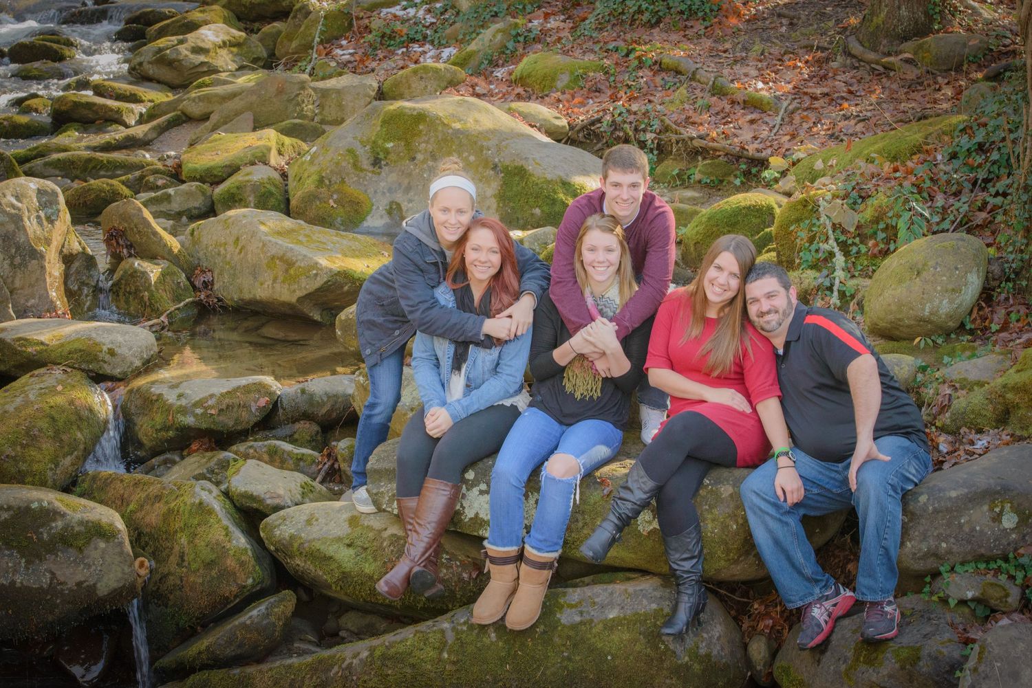 A group sits together on mossy rocks outdoors during an autumn photoshoot in nature by Sevierville TN photographer.