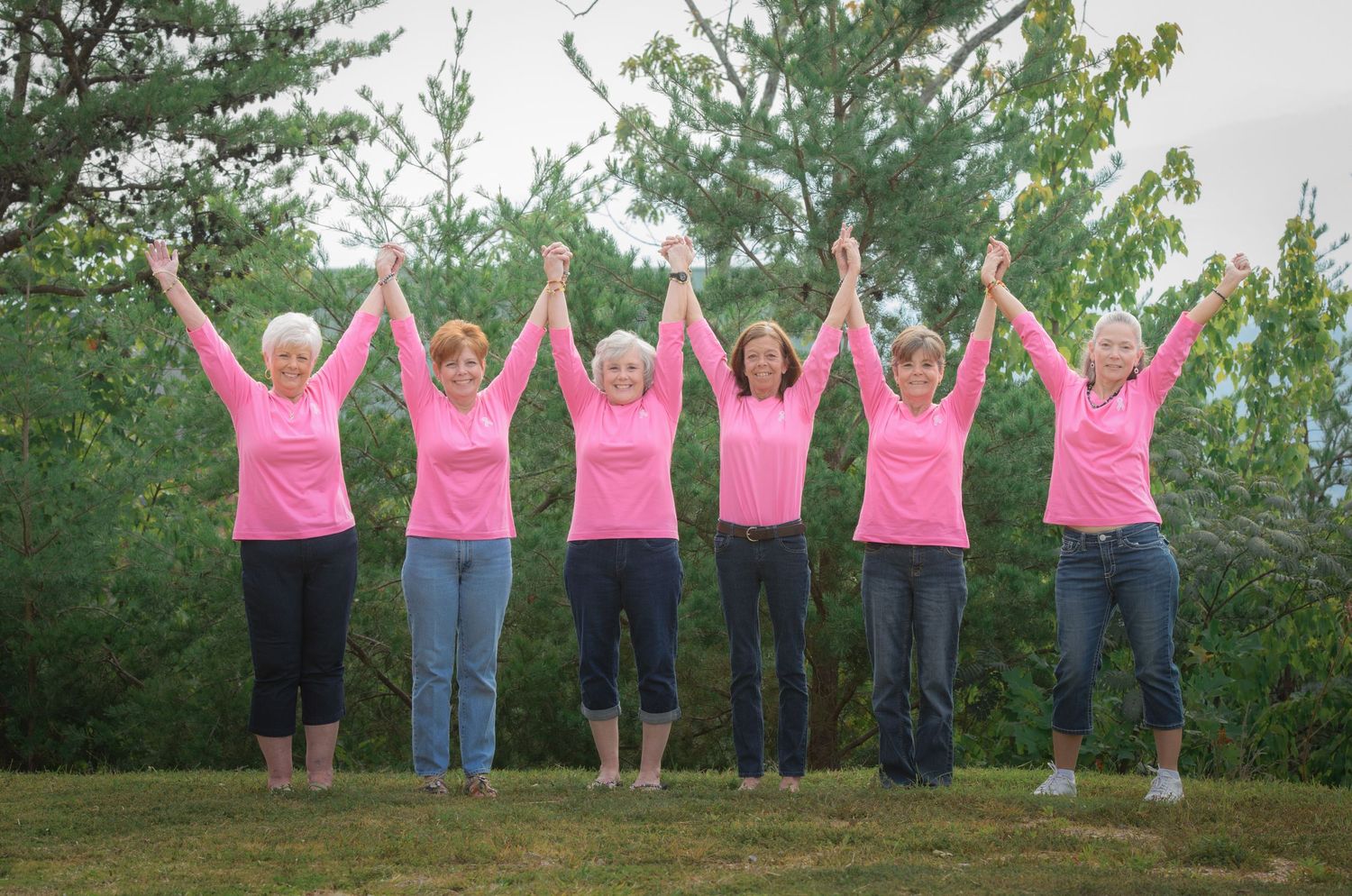 A group of sisters wearing breast cancer awareness shirts against green tress by Gatlinburg Photographers TN.