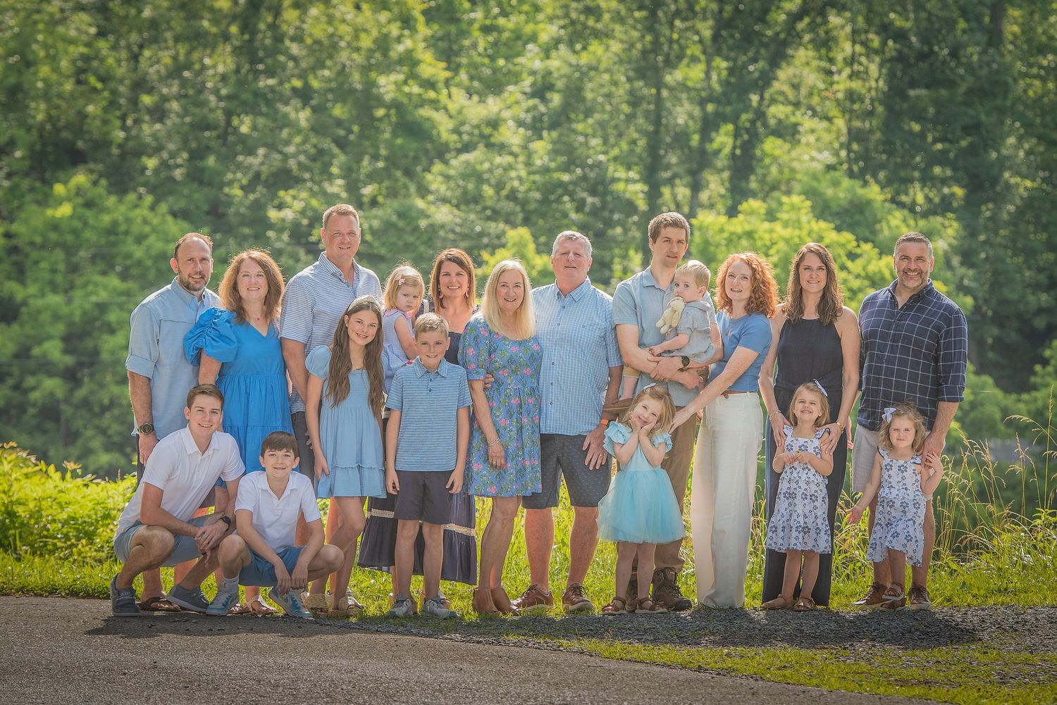 Large reunion wearing coordinated blue and white outfits poses together outdoors in front of sunny green foliage in Gatlinburg TN.