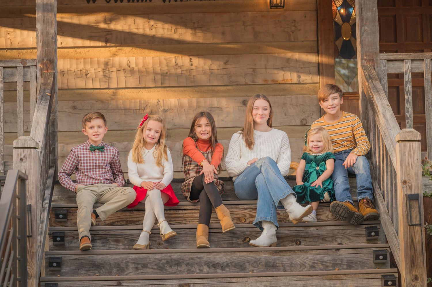 Five young people sit casually together on wooden porch steps during golden hour.