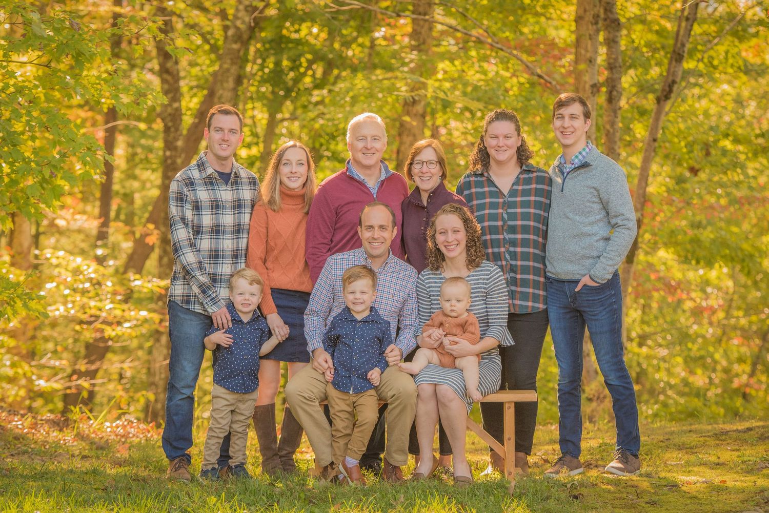 A happy family poses together outdoors against autumn foliage in a sunny wooded setting by Pigeon Forge Photographers.