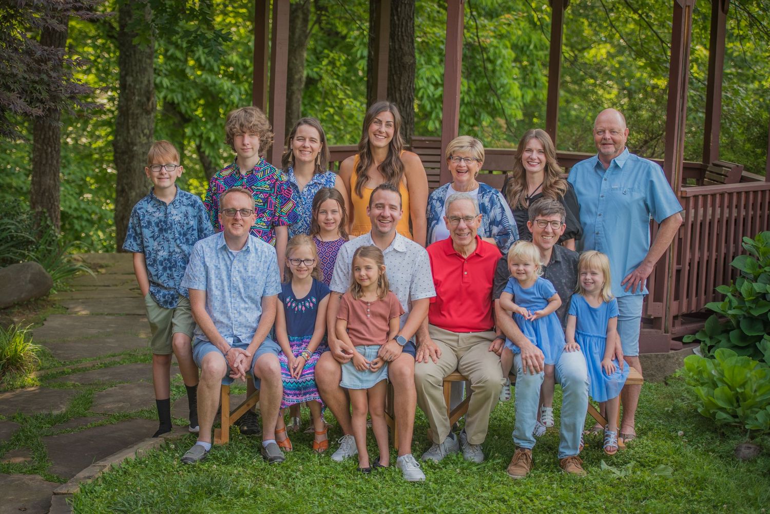 A family reunion coordinated in blue and red casual outfits poses together on an outdoor deck surrounded by lush green trees Pigeon Forge TN