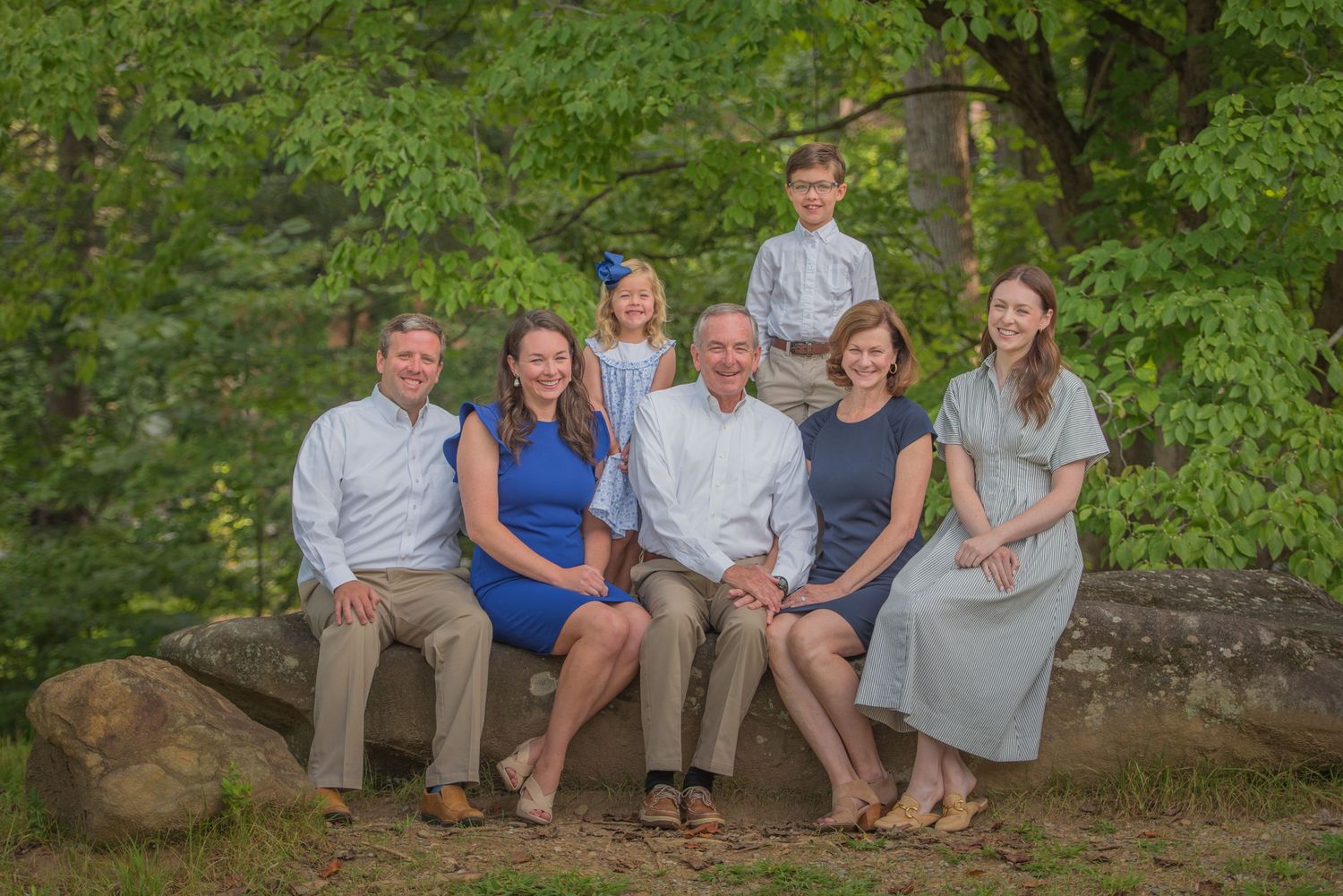 Family group portrait sitting together on a large rock outdoors with green foliage background in summer in Gatlinburg TN.