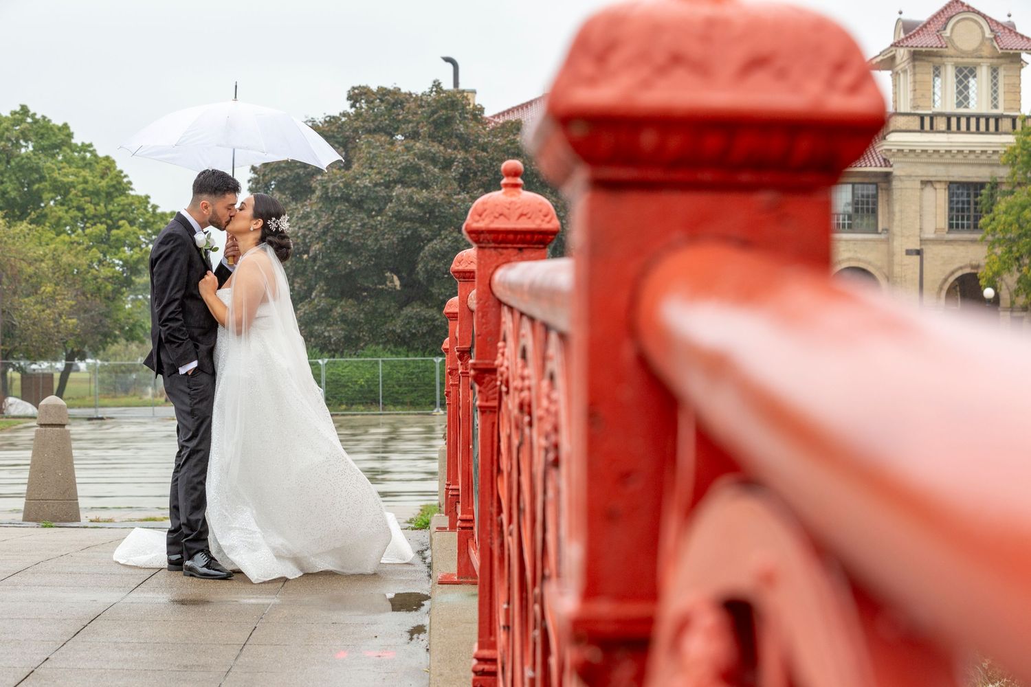 A romantic moment captured beside bright red railings at a scenic outdoor location on a misty day.