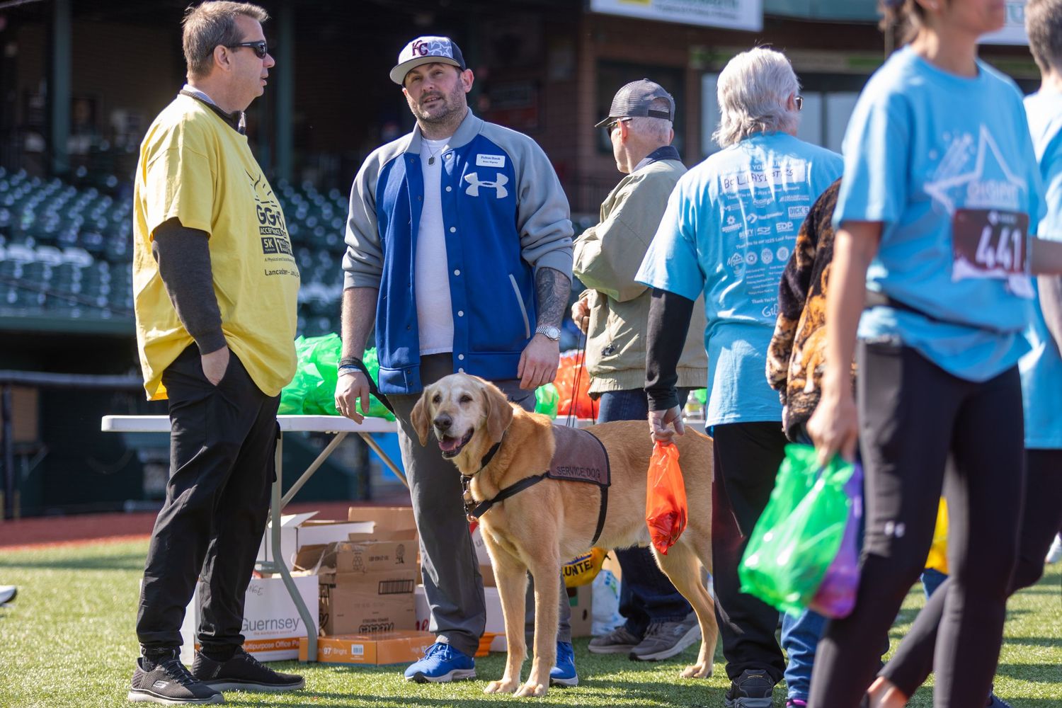 People and a friendly golden retriever gather on a field during an outdoor community event.