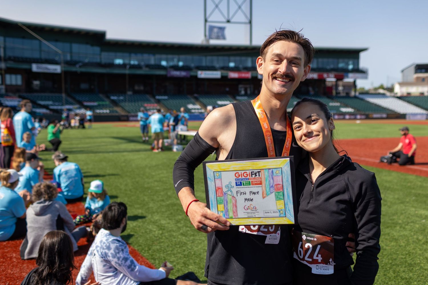 Two people hold up an achievement certificate at an outdoor sporting event.