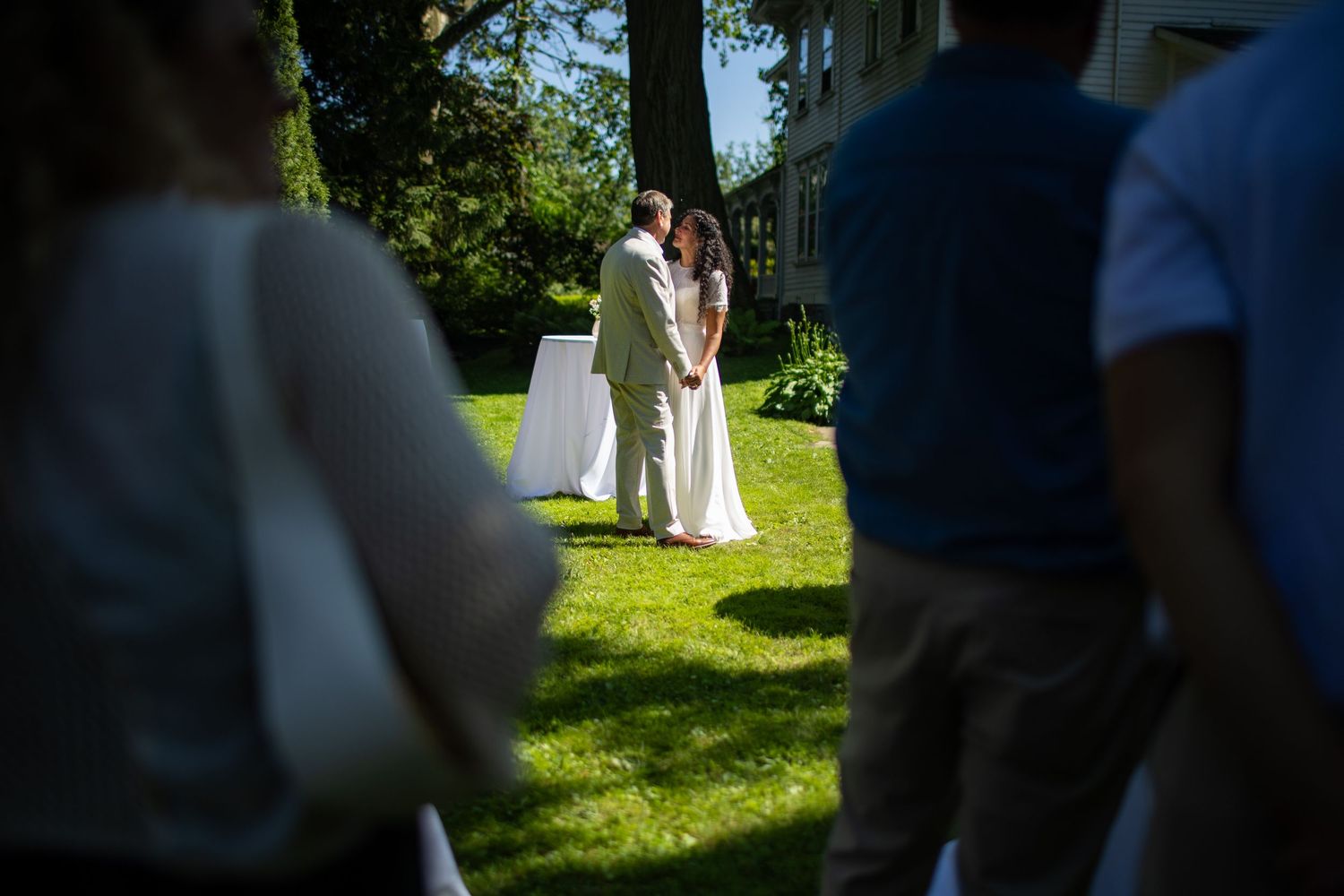 A garden wedding ceremony takes place on a sunny day with guests gathered on a lush green lawn.