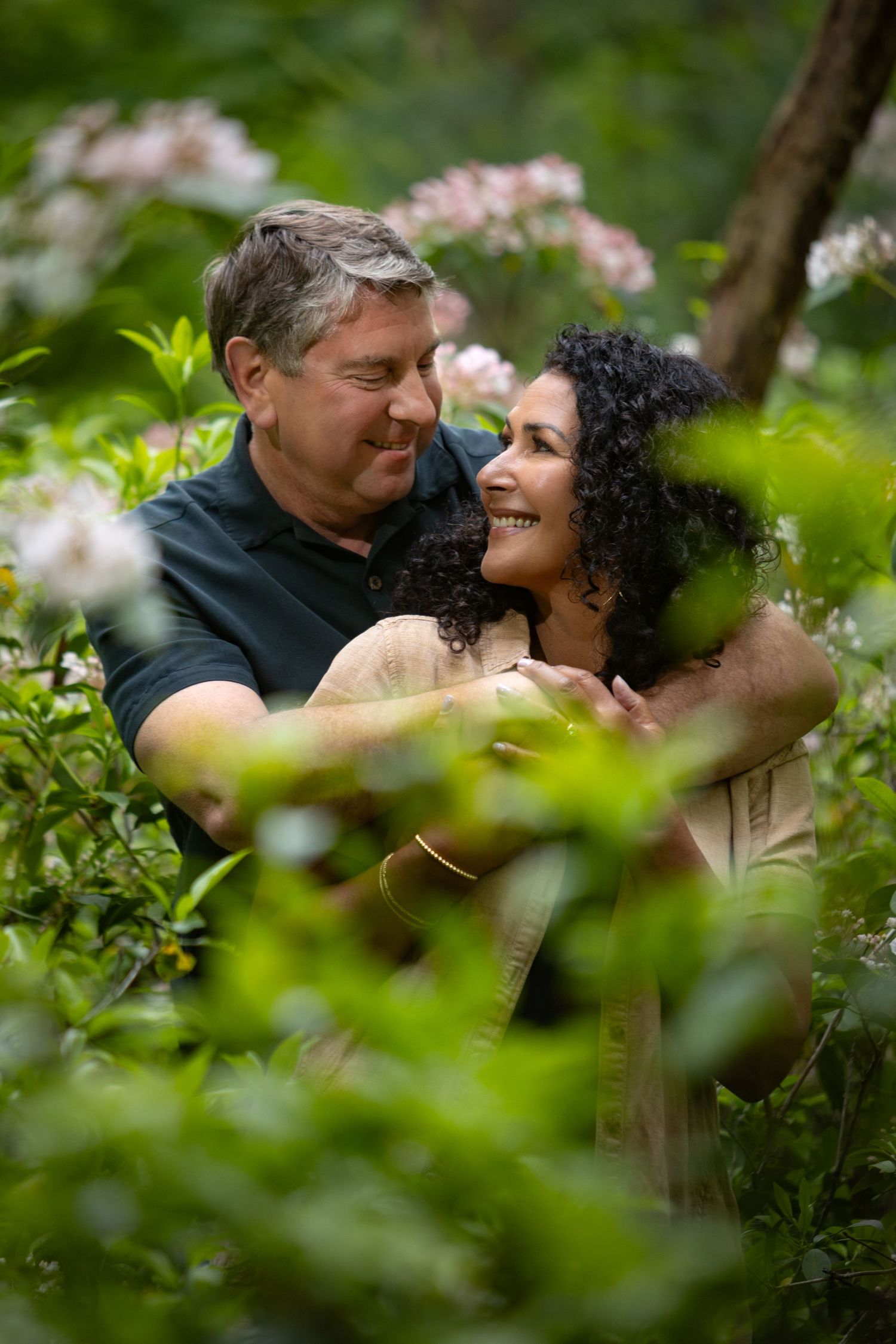 A couple shares an intimate embrace surrounded by blooming flowers and lush greenery in a garden setting.
