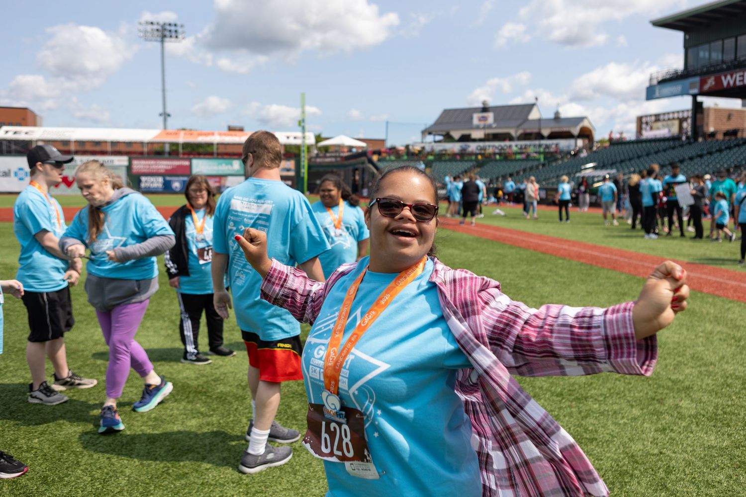 Participants in light blue shirts gather on a baseball field during a sunny outdoor event.