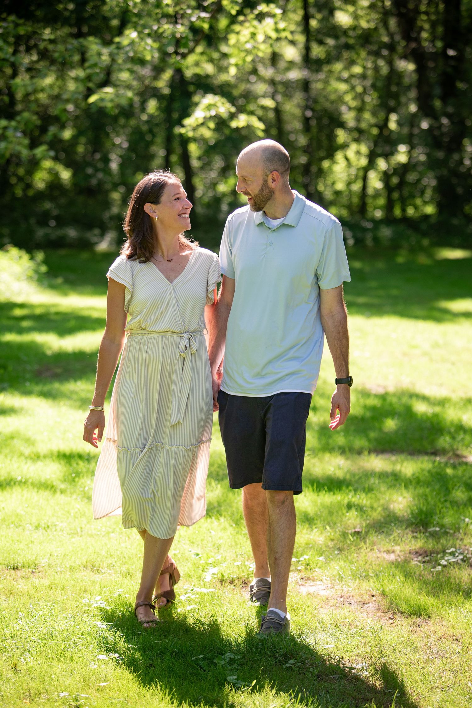 A couple walks together through a sunlit park on a summer day, laughing and enjoying each other's company.