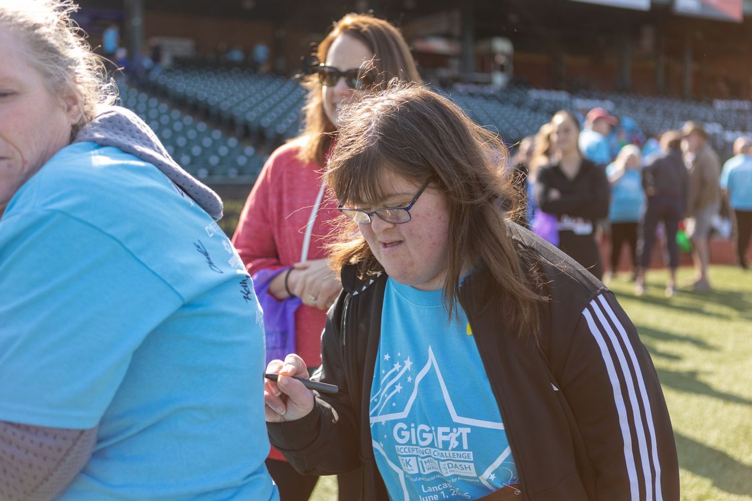 Participants in light blue shirts gather on baseball field during community event.