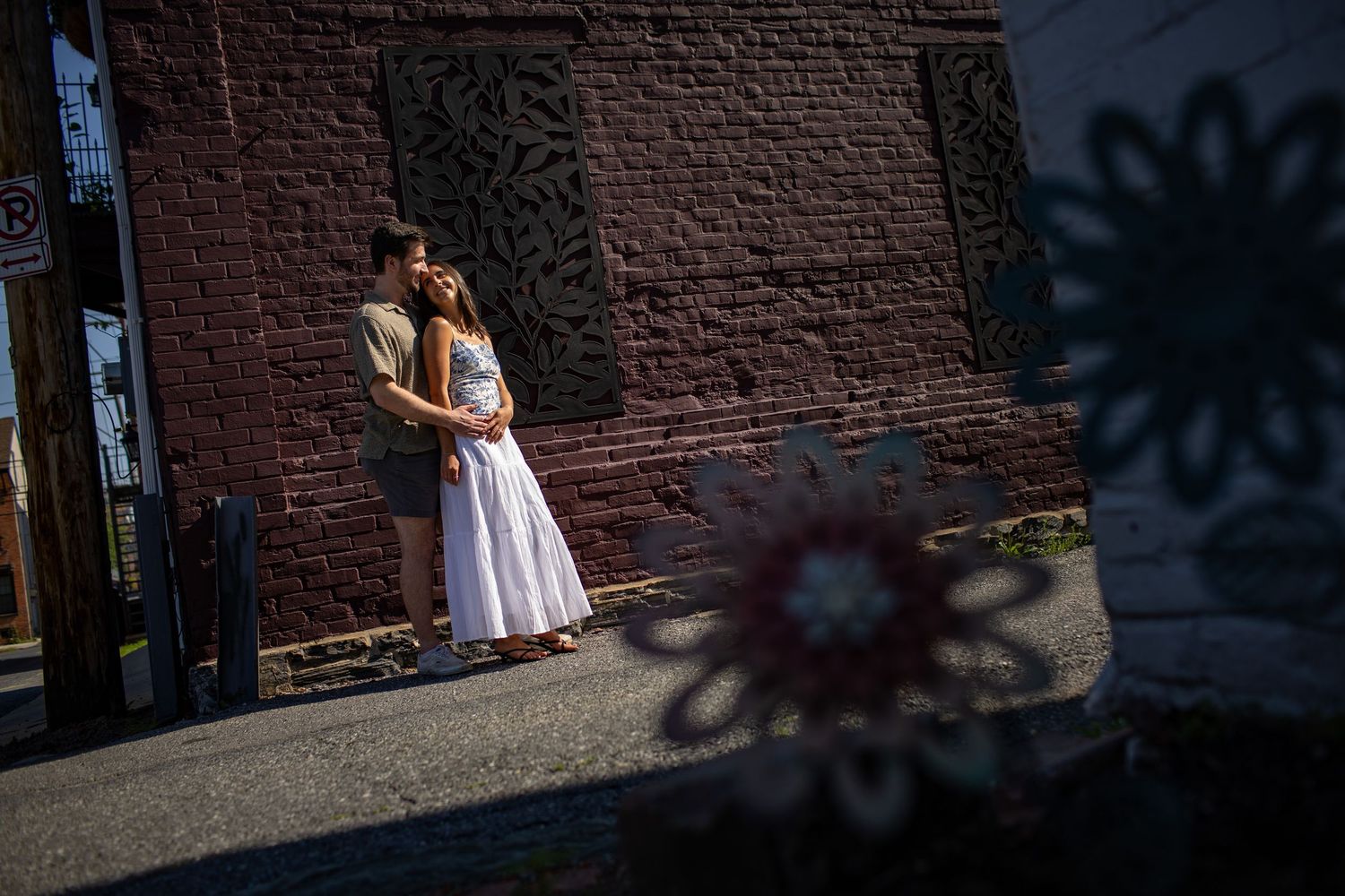 A woman in a white dress twirls and dances against a rustic brick wall in natural sunlight.