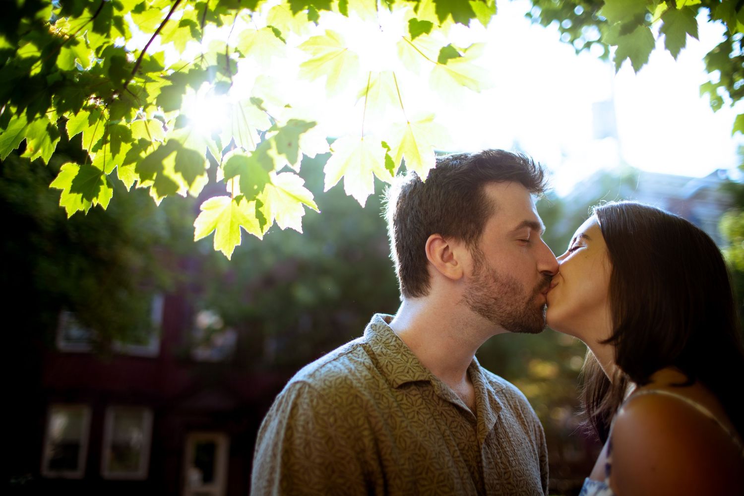 Romantic couple sharing an intimate moment under sunlit tree branches at golden hour.