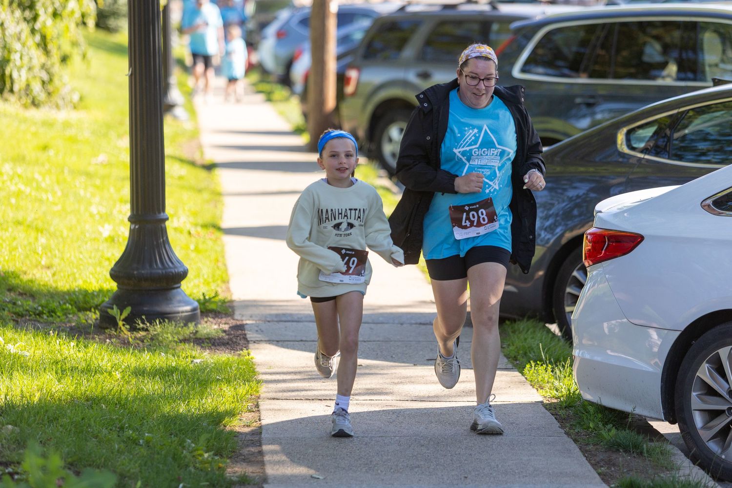 Participants jog along a sidewalk during a community running event.