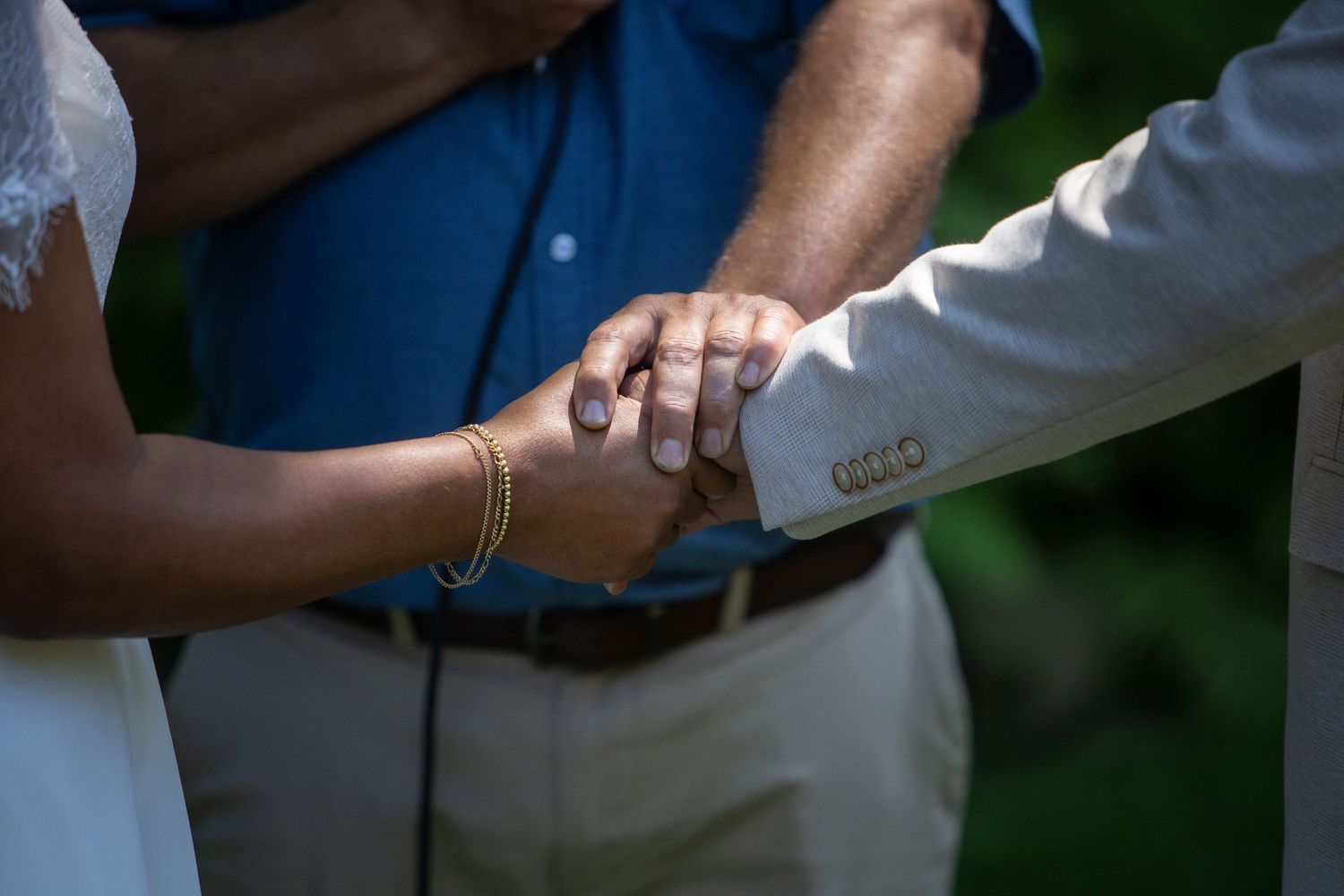 Close up detail of hands clasped together during a wedding ceremony ritual in an outdoor setting.