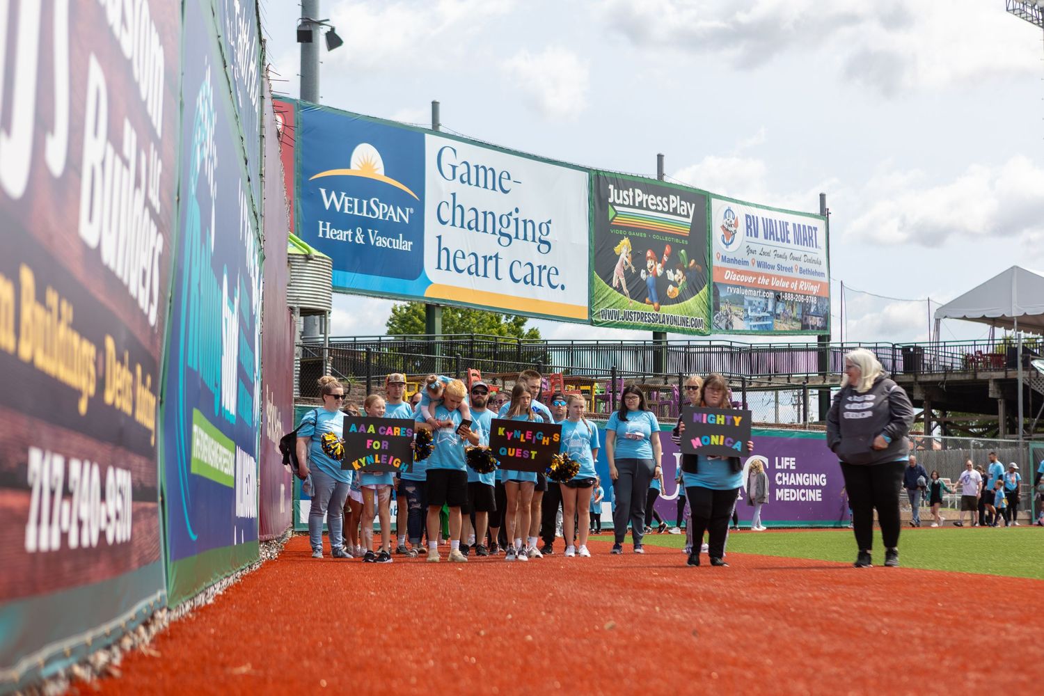Group of participants gathered at starting line for charity walk event at baseball stadium.