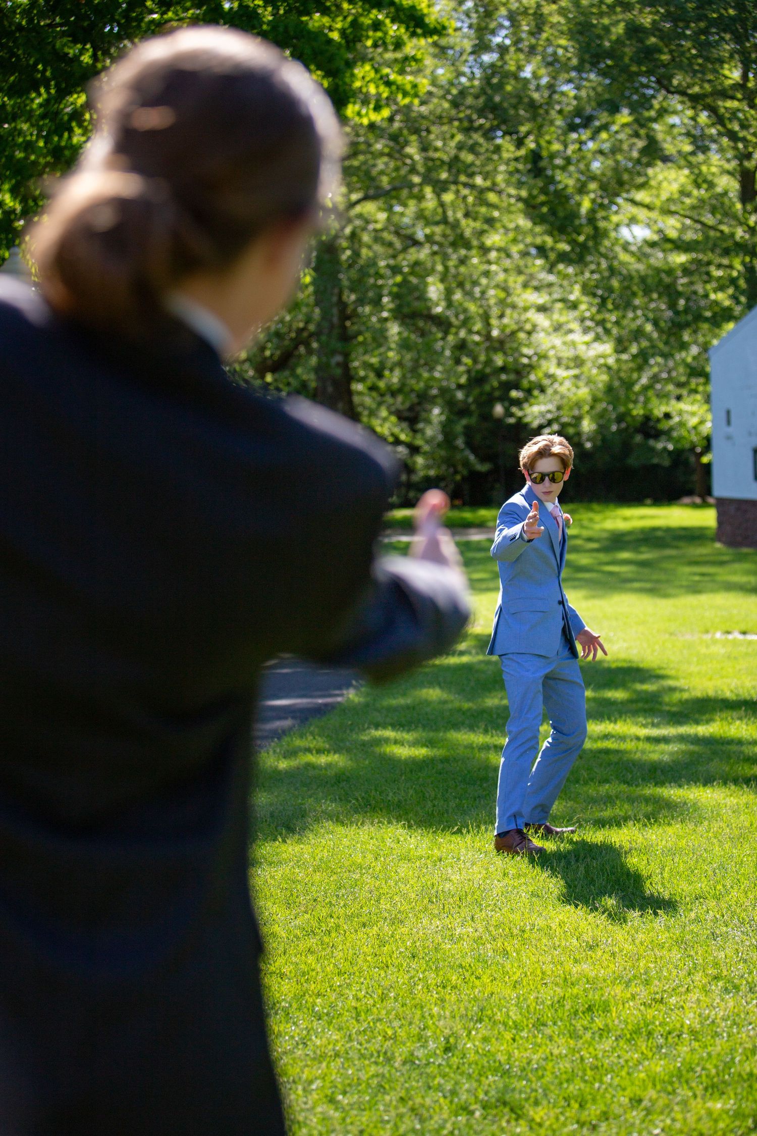 People in bright sunlight enjoying outdoor activities on a grassy lawn surrounded by green trees on a summer day.
