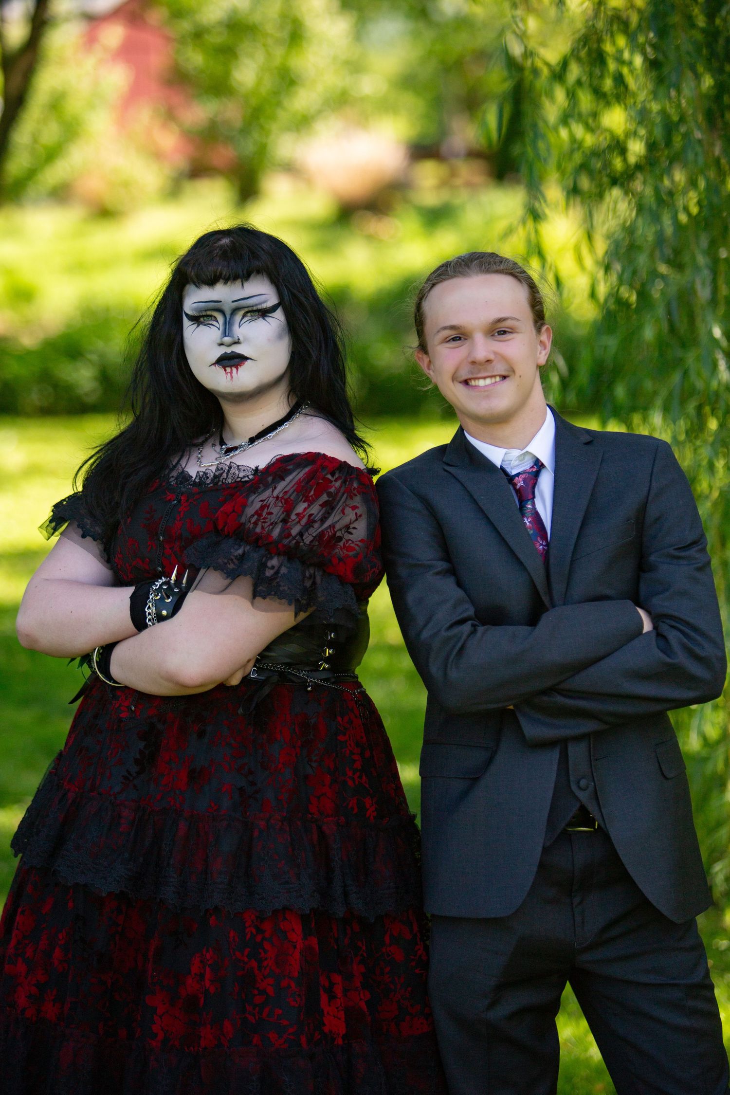 A contrasting couple poses outdoors - one in gothic red and black dress, the other in traditional business suit.