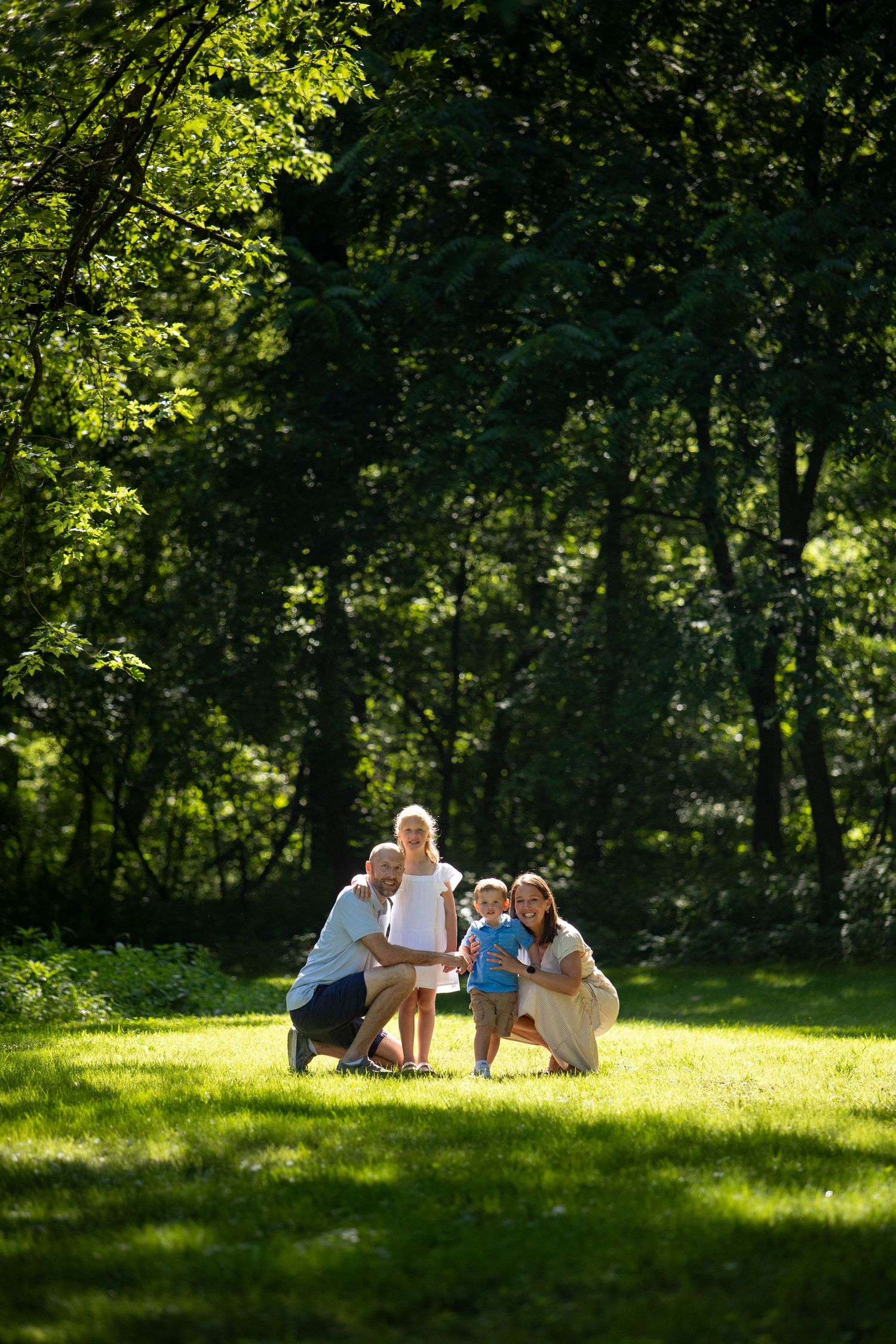 Family relaxing together on a grassy hillside in a sunlit park on a summer afternoon.