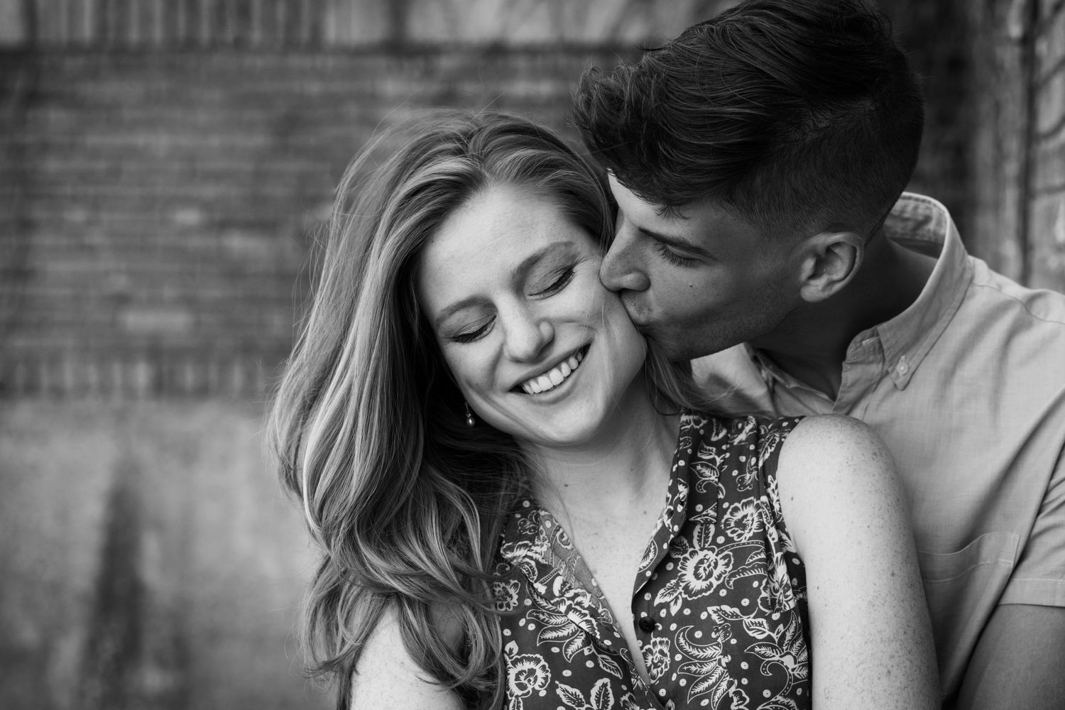 Romantic black and white portrait of couple sharing tender moment against brick wall.