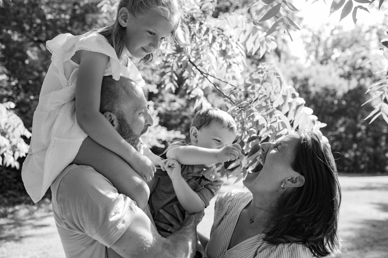 A candid black and white moment of a family playing and laughing together outdoors in a garden setting.