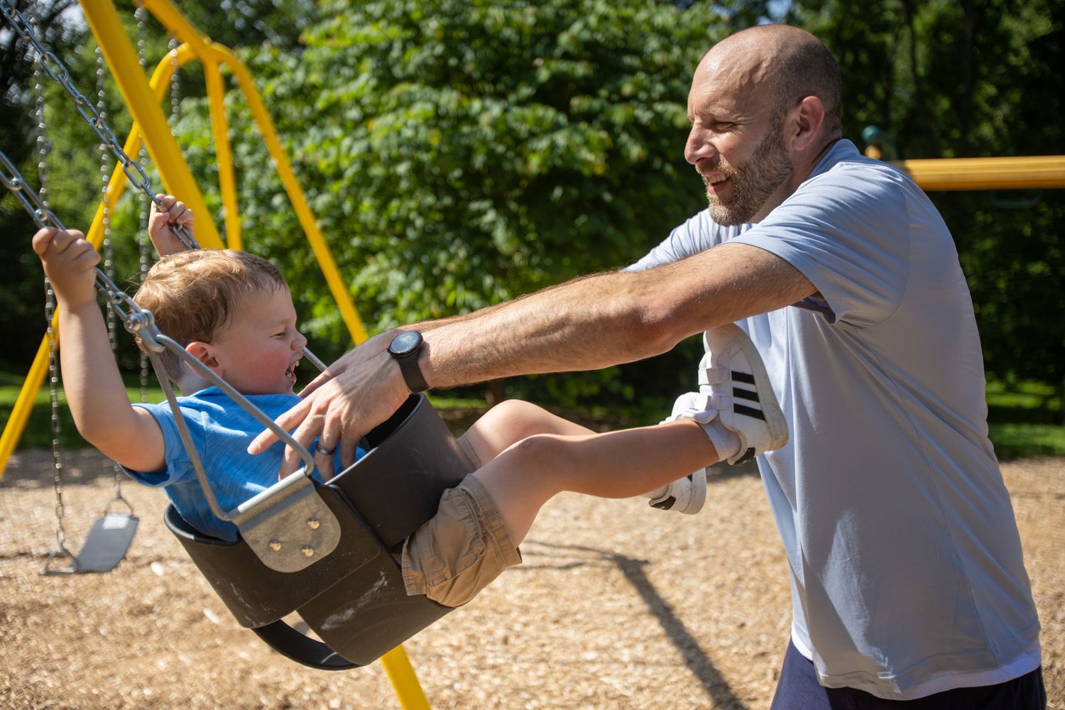 A parent pushes a happy child in a swing at a sunny playground, creating joyful outdoor memories together.
