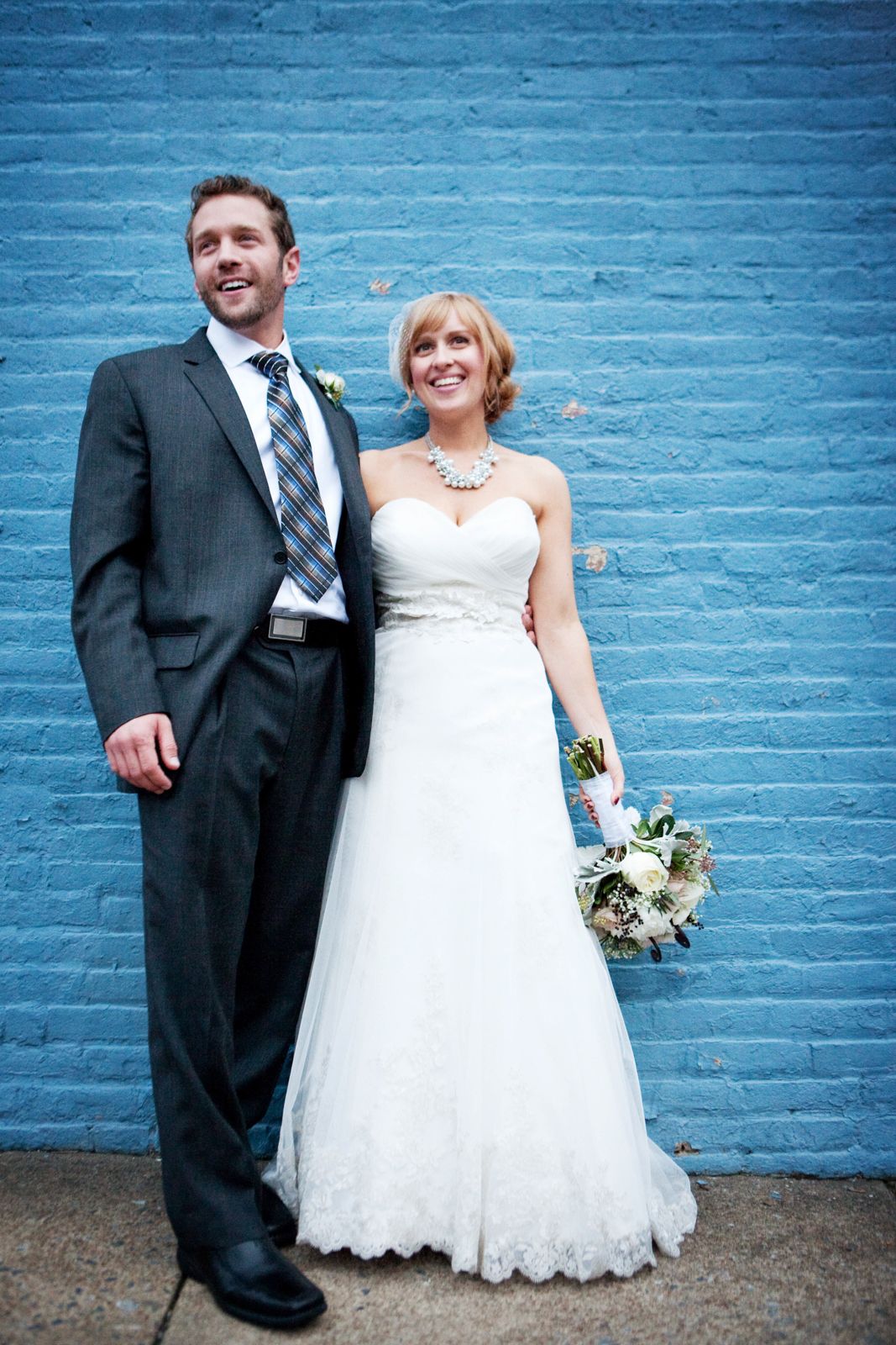 A bride and groom pose together against bright blue painted brick wall in a series of candid moments.