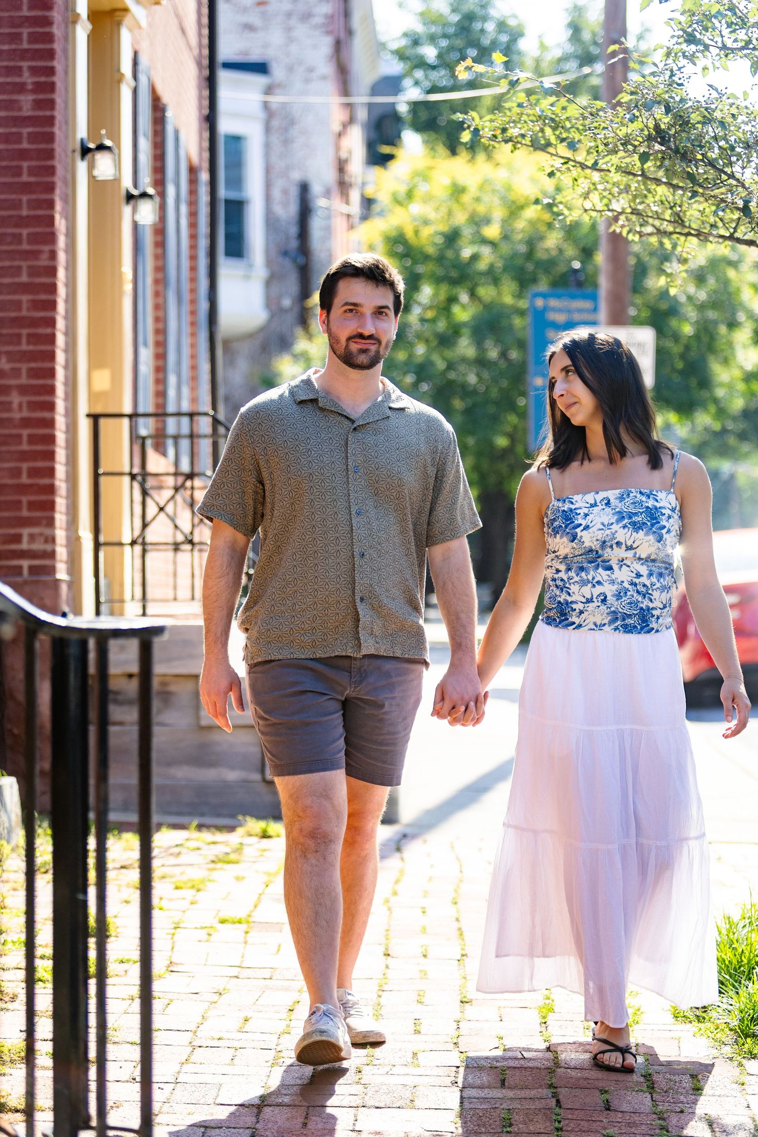 A couple walking together on a brick sidewalk in warm summer clothing on a sunny afternoon.