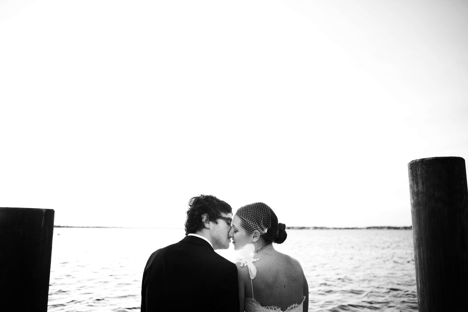 Silhouette of newlyweds sharing intimate kiss by waterfront during sunset.