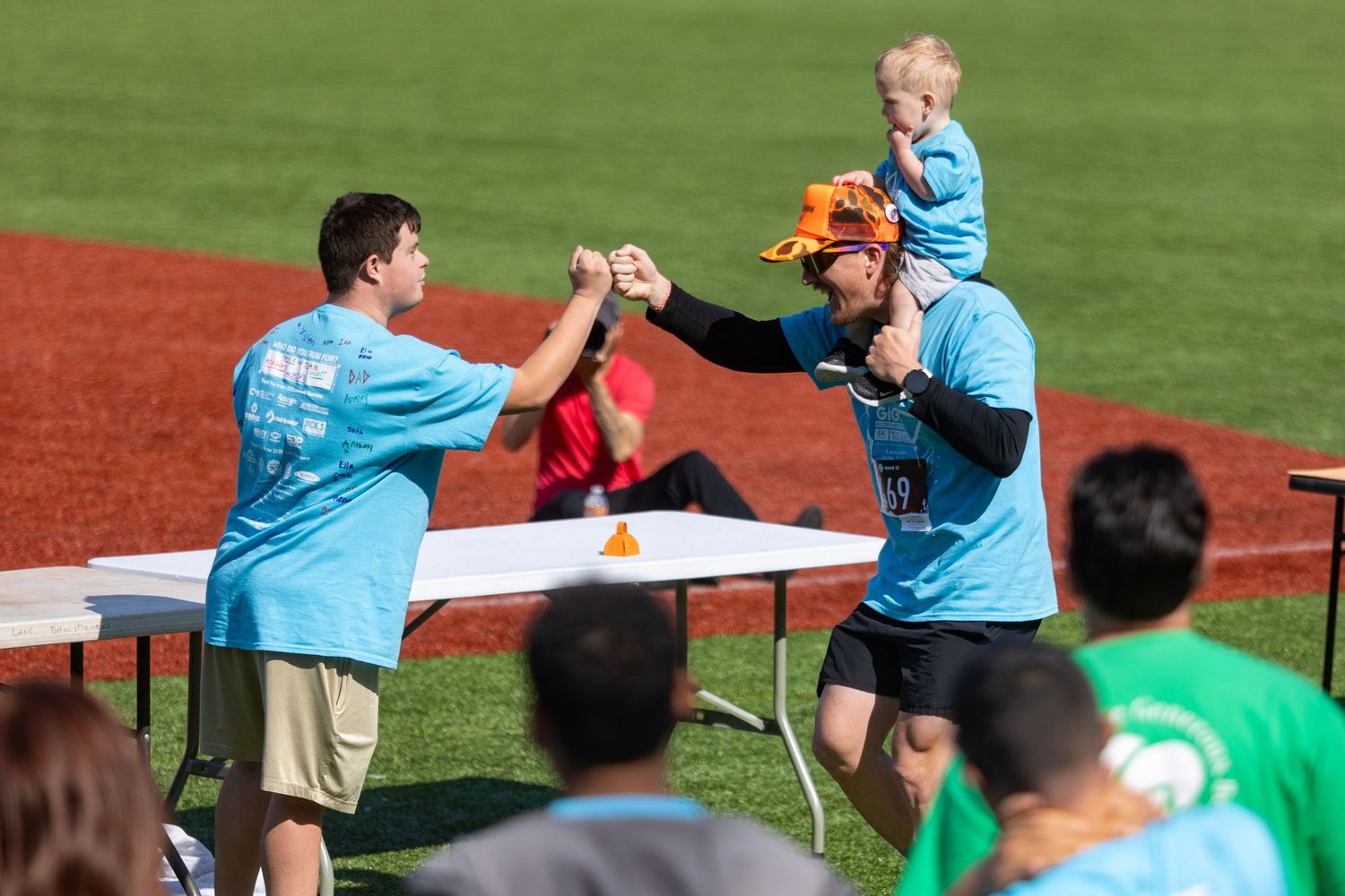 Volunteers in light blue shirts celebrate with high fives at an outdoor sporting event.
