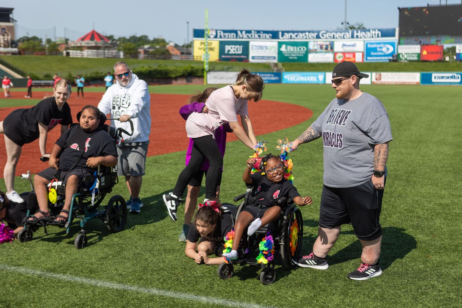 Group gathering around mobility equipment on baseball field grass.