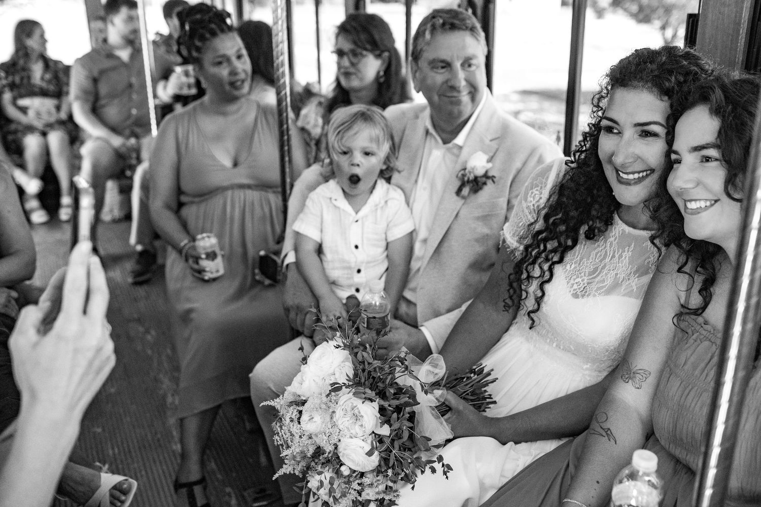 A joyful black and white wedding photo of couples and guests celebrating on a trolley.