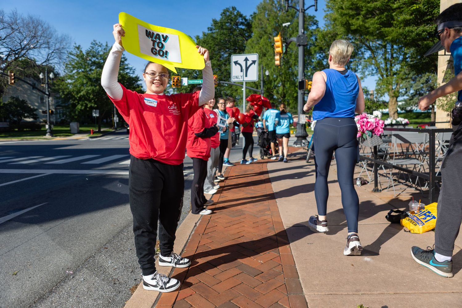 Participant holding yellow sign while cheering along sidewalk during community event.