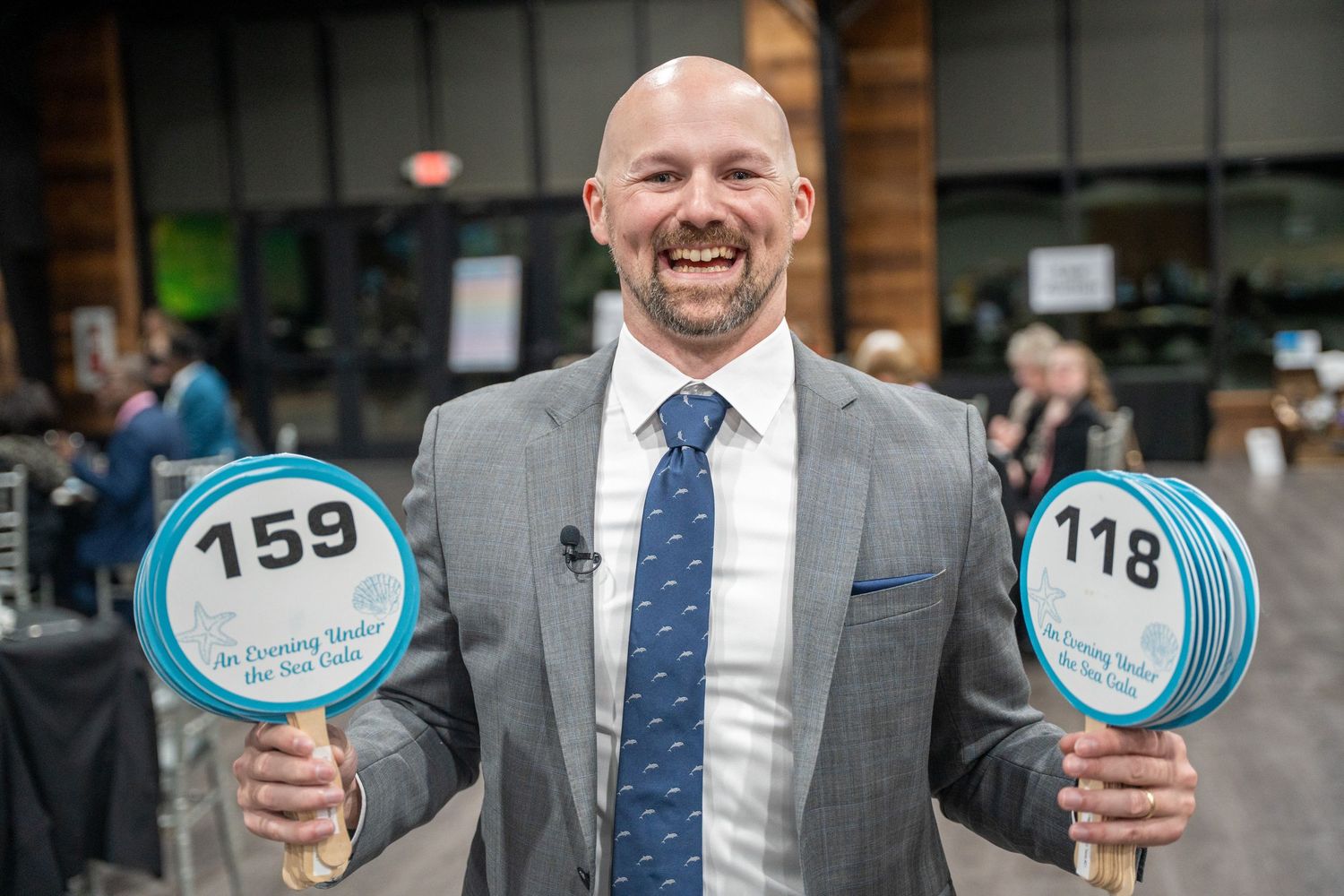 Formal portraits of businessmen in gray suits with ties holding numbered auction paddles with smiles.