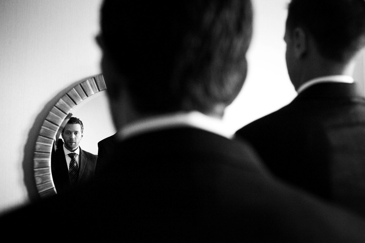 Dramatic black and white reflection in mirror shows silhouetted figures with one person visible through narrow curved frame.