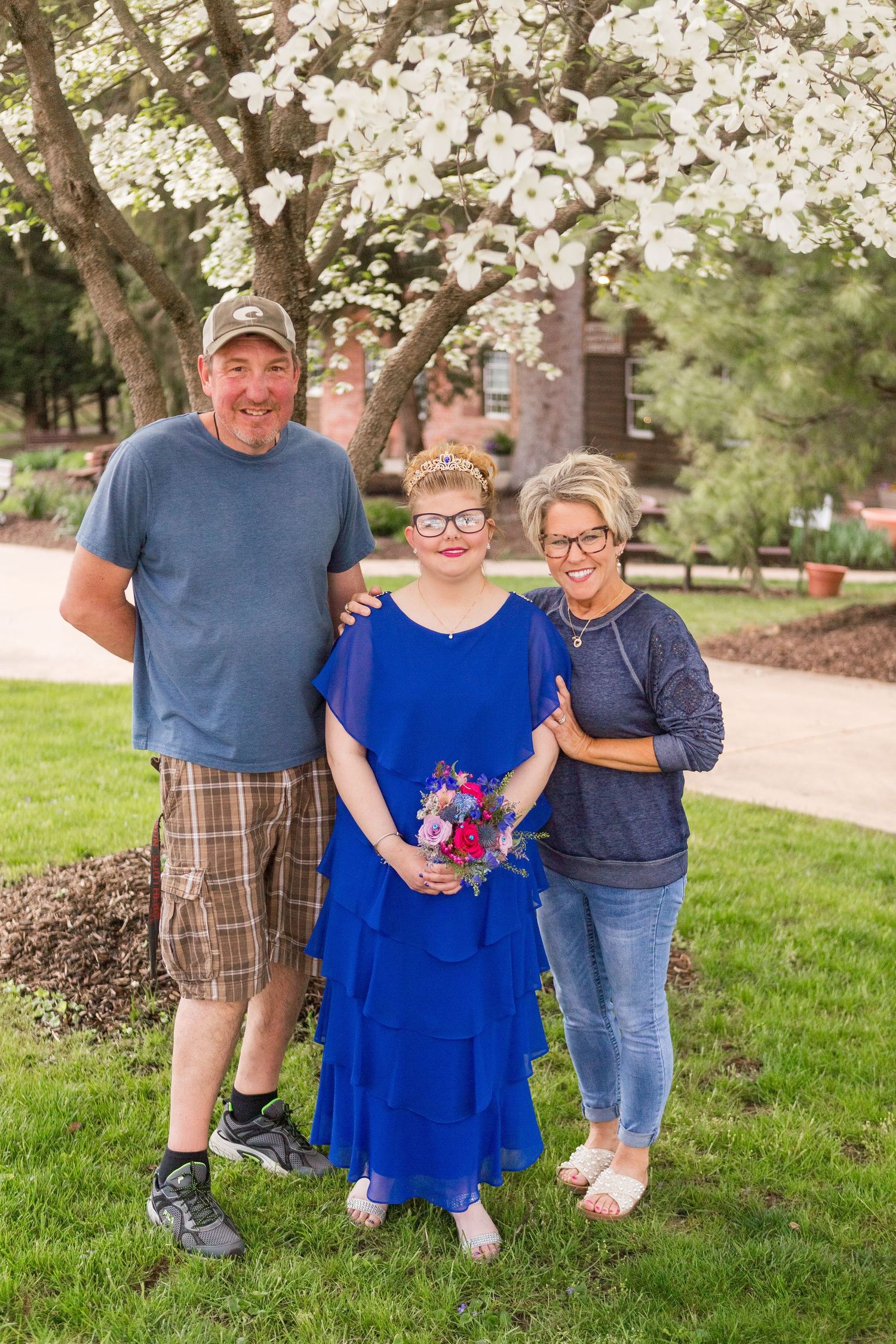 Family portrait under blooming cherry trees with person in blue dress holding flowers.