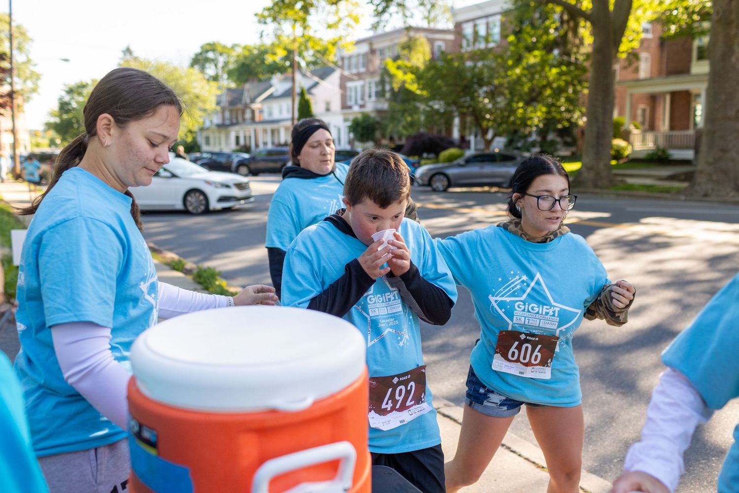 People in matching blue t-shirts participate in an outdoor event with tables set up along a sunny path.