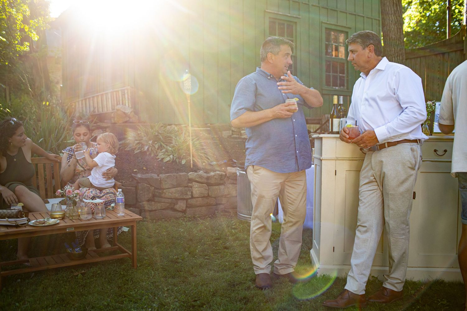 Two people having a conversation at an outdoor party in a backyard with warm sunlit atmosphere.