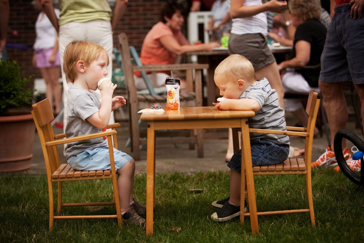 Two young children sitting at a wooden table outdoors at a casual dining event.